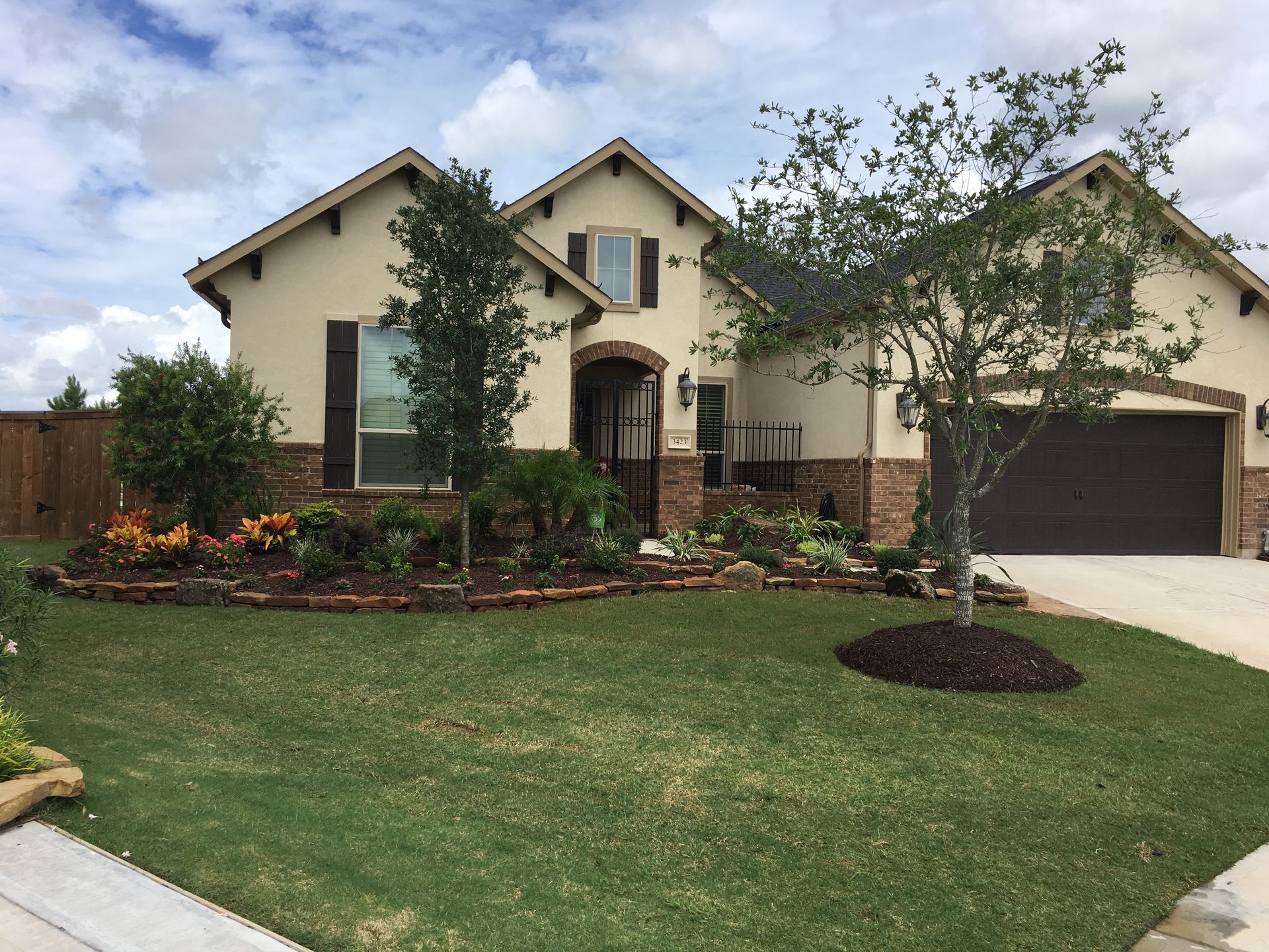 Suburban single-story house with stone entry, garage, manicured lawn, and landscaped front yard