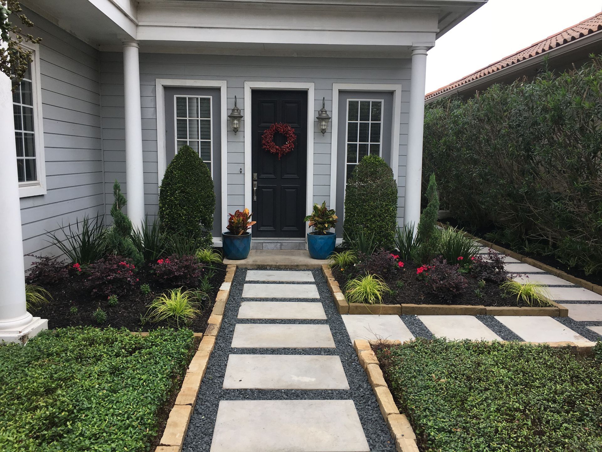 Front porch with a dark door, potted plants, and a stone walkway leading through a manicured front yard