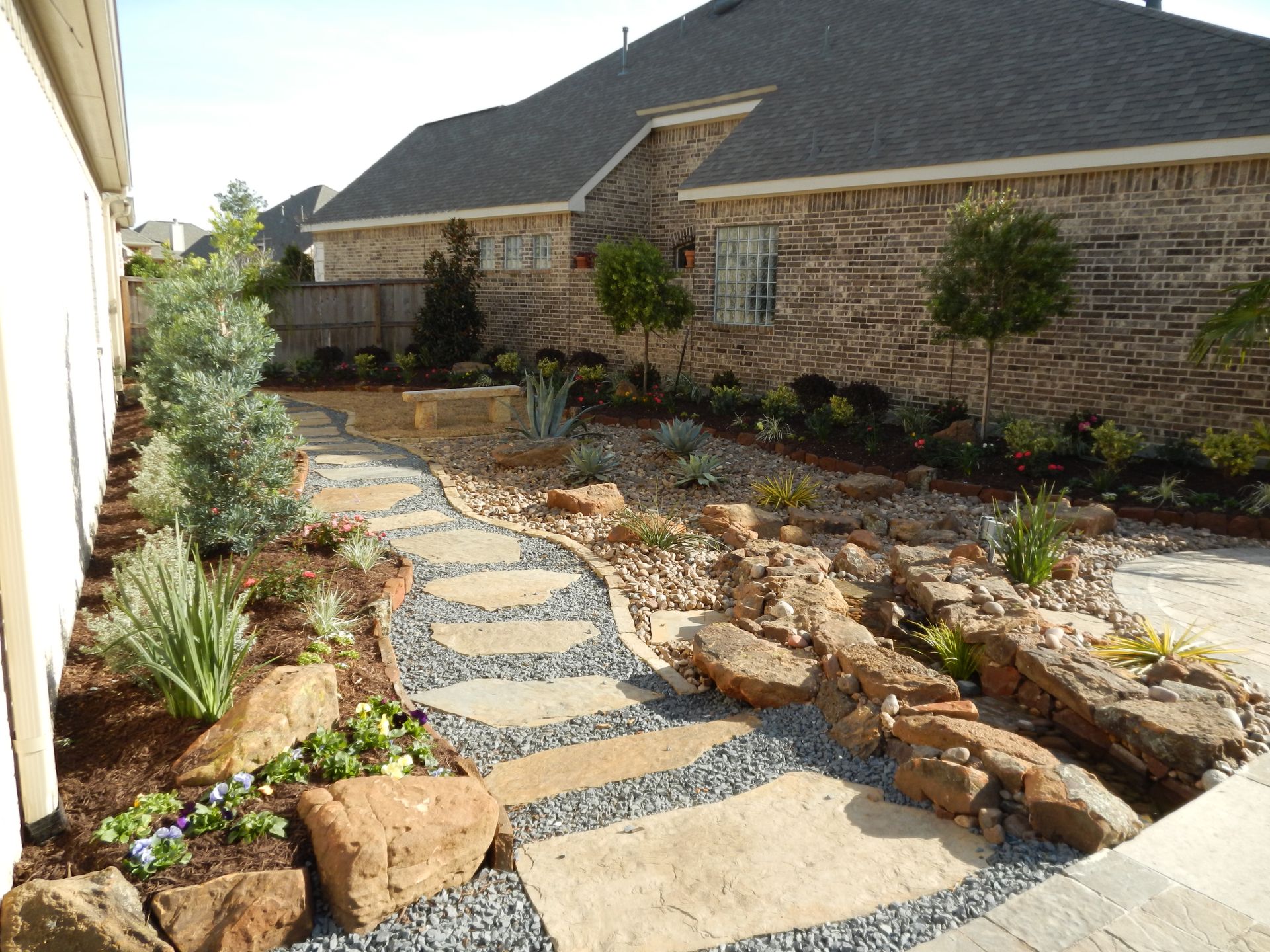 Stepping-stone garden path beside a stone house, lined with rocks and shrubs