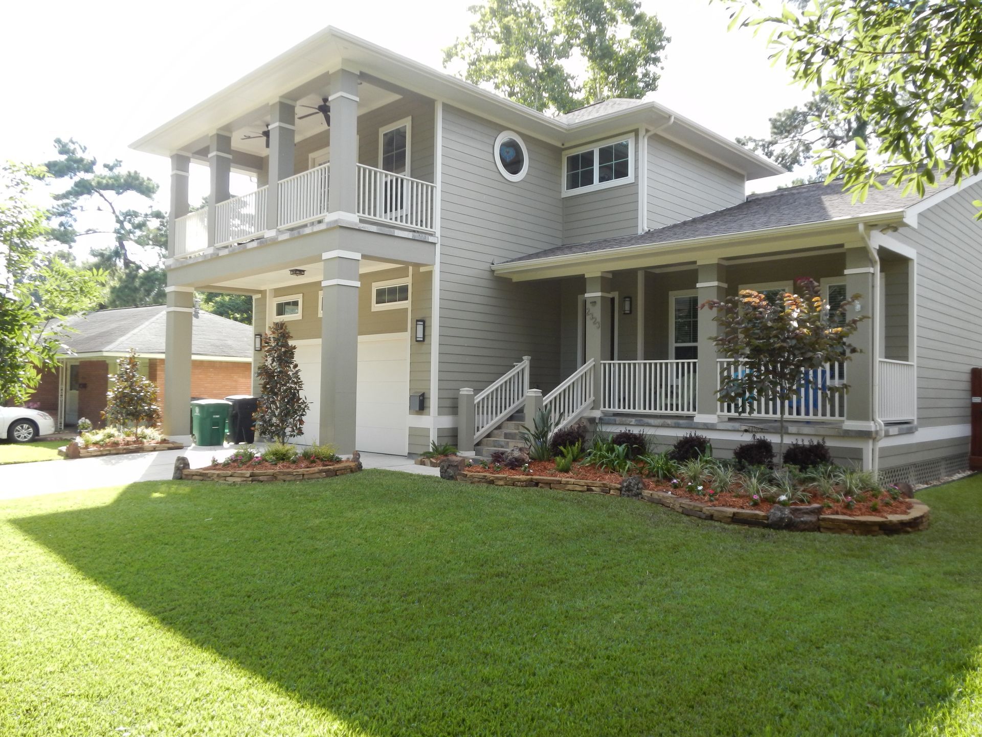 Two-story gray house with a white porch and a green lawn under bright sunlight