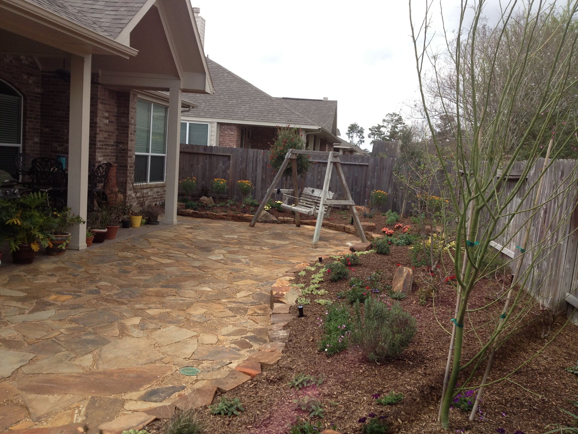Backyard patio with stone paving, a swing set, garden beds, and a house exterior.