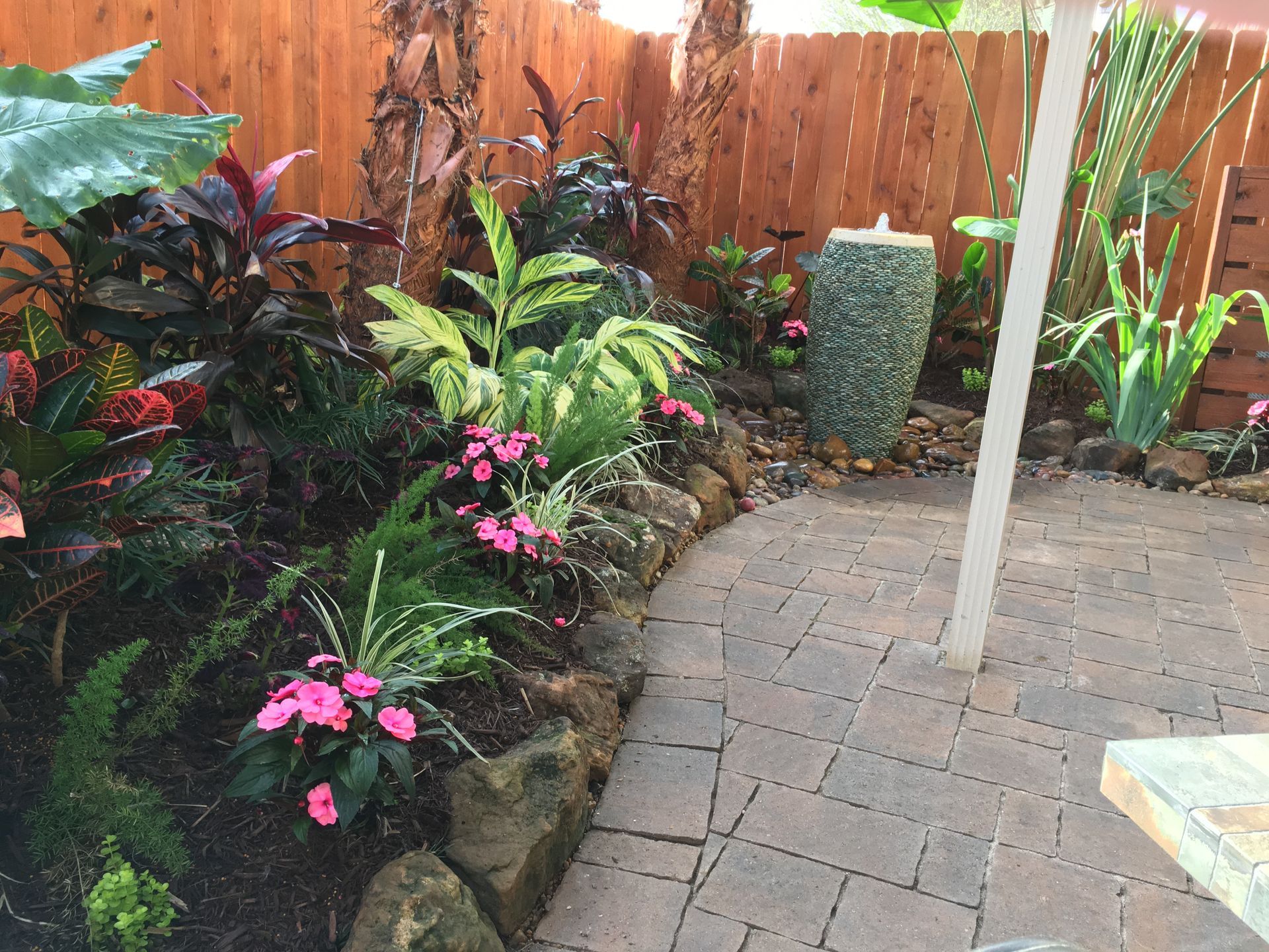 Tropical garden path with colorful plants, brick paving, and a wooden fence
