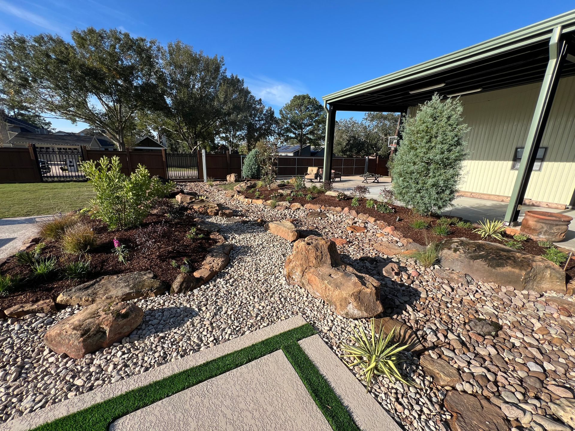 Desert-style front yard with gravel, rocks, shrubs, and a covered patio under a blue sky