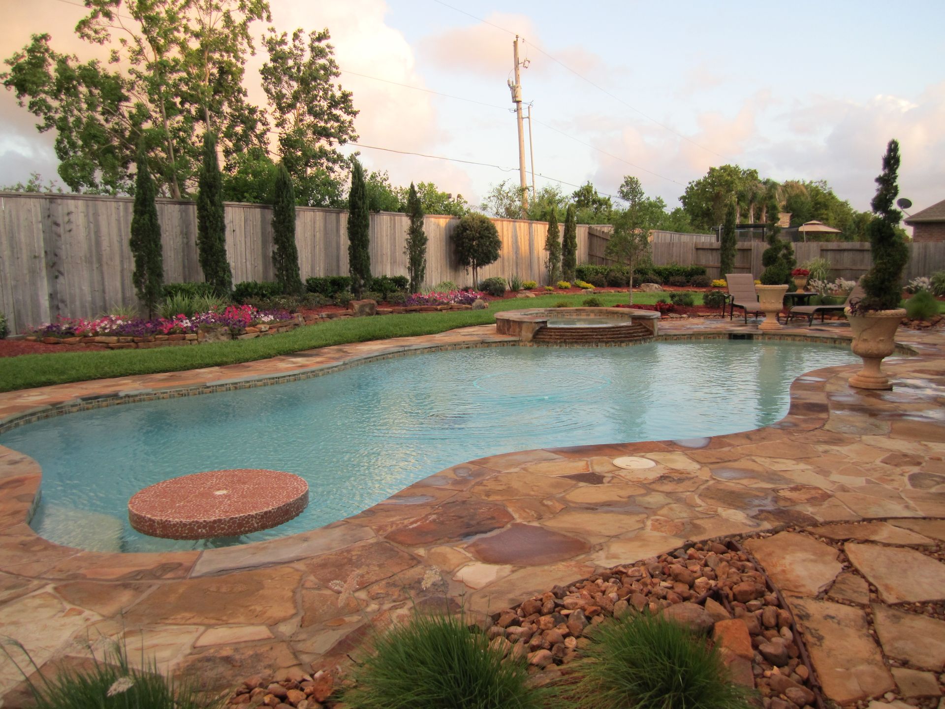 Backyard pool with stone deck, landscaped border, and a round floating stepping stone