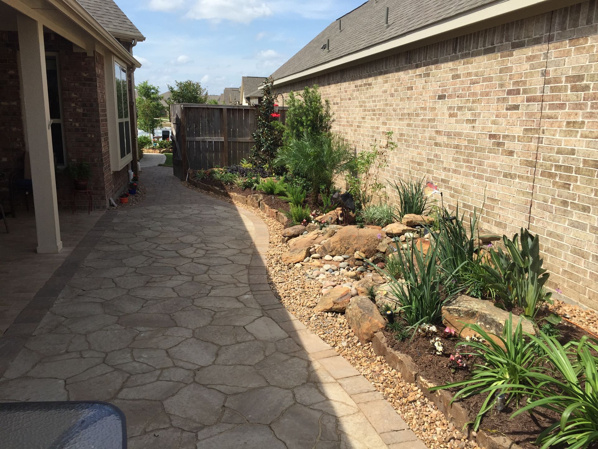 Narrow stone walkway beside a brick house, lined with a small rock garden and plants.