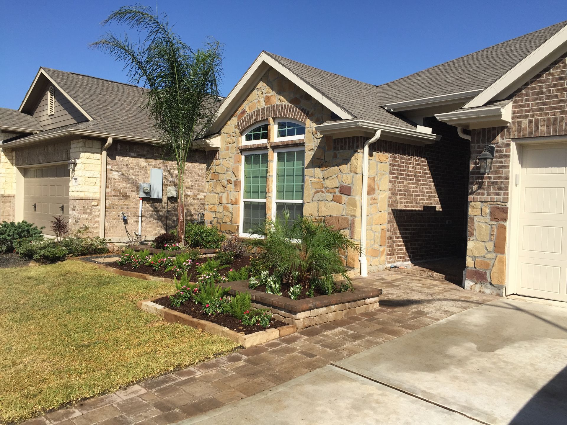 Suburban brick house with front walkway, landscaped garden, and a beige garage door