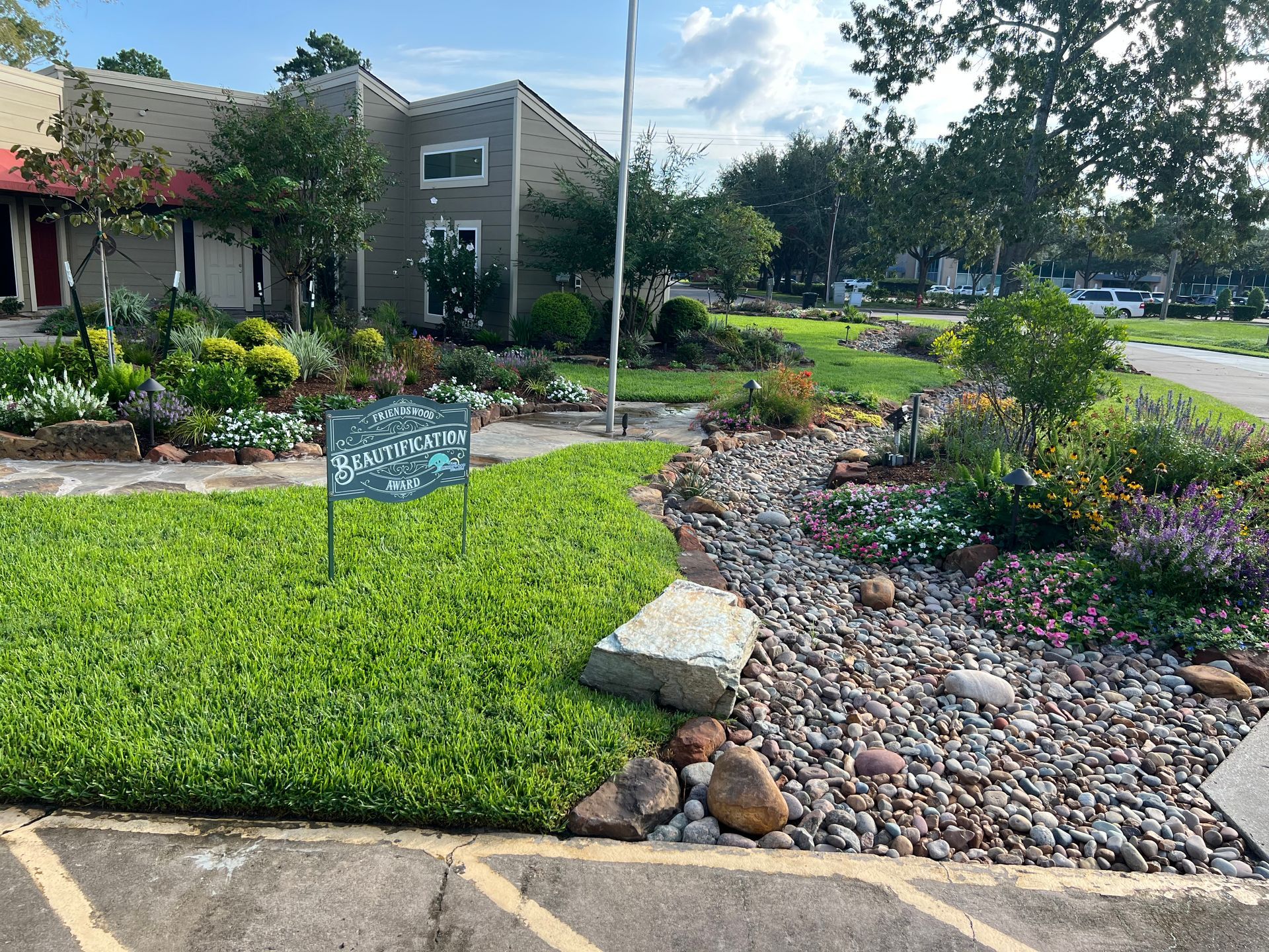 Landscaped front yard with flowers, rocks, and a sign near a residential building