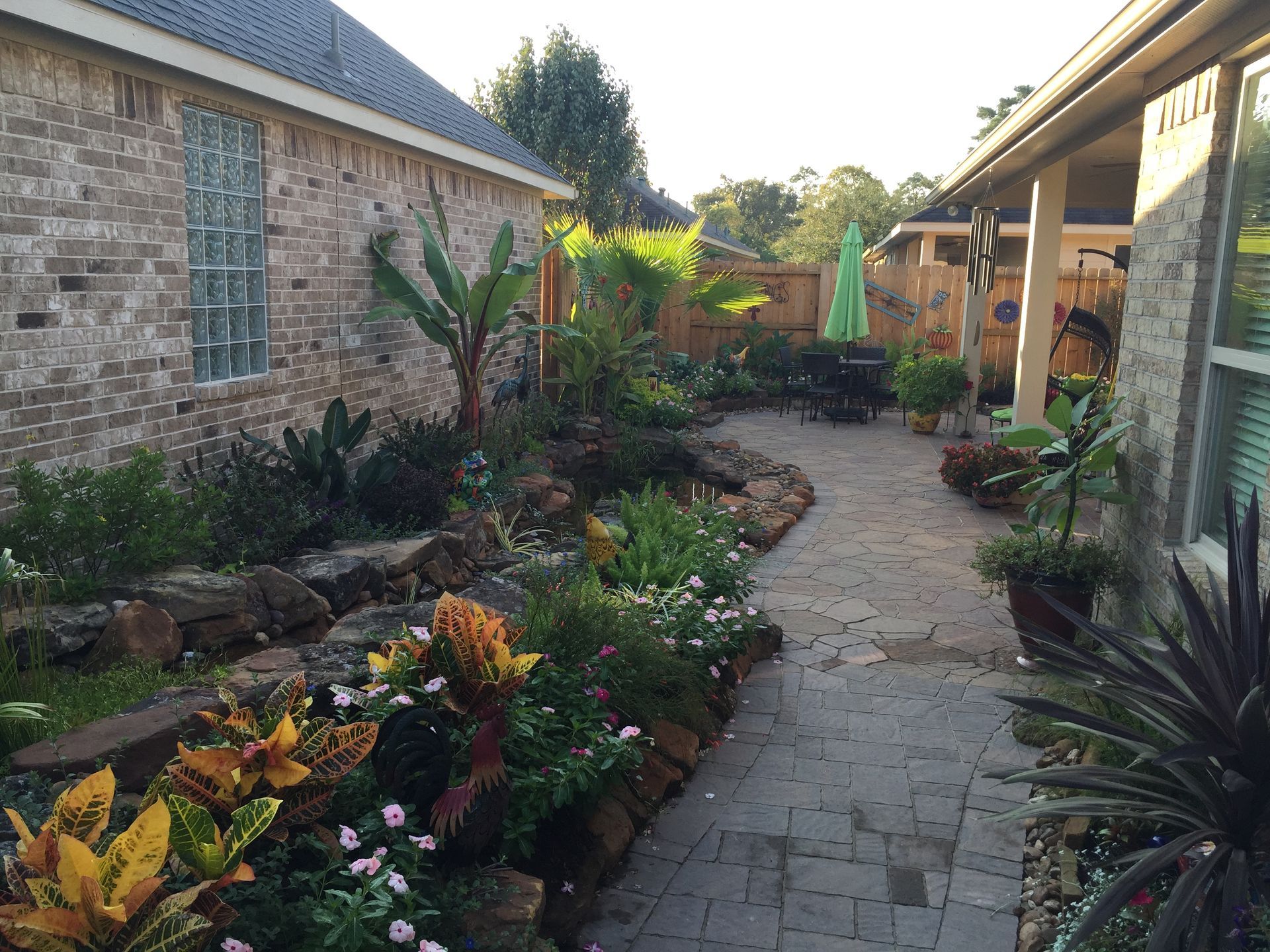 Brick house garden path with colorful plants and a covered patio area