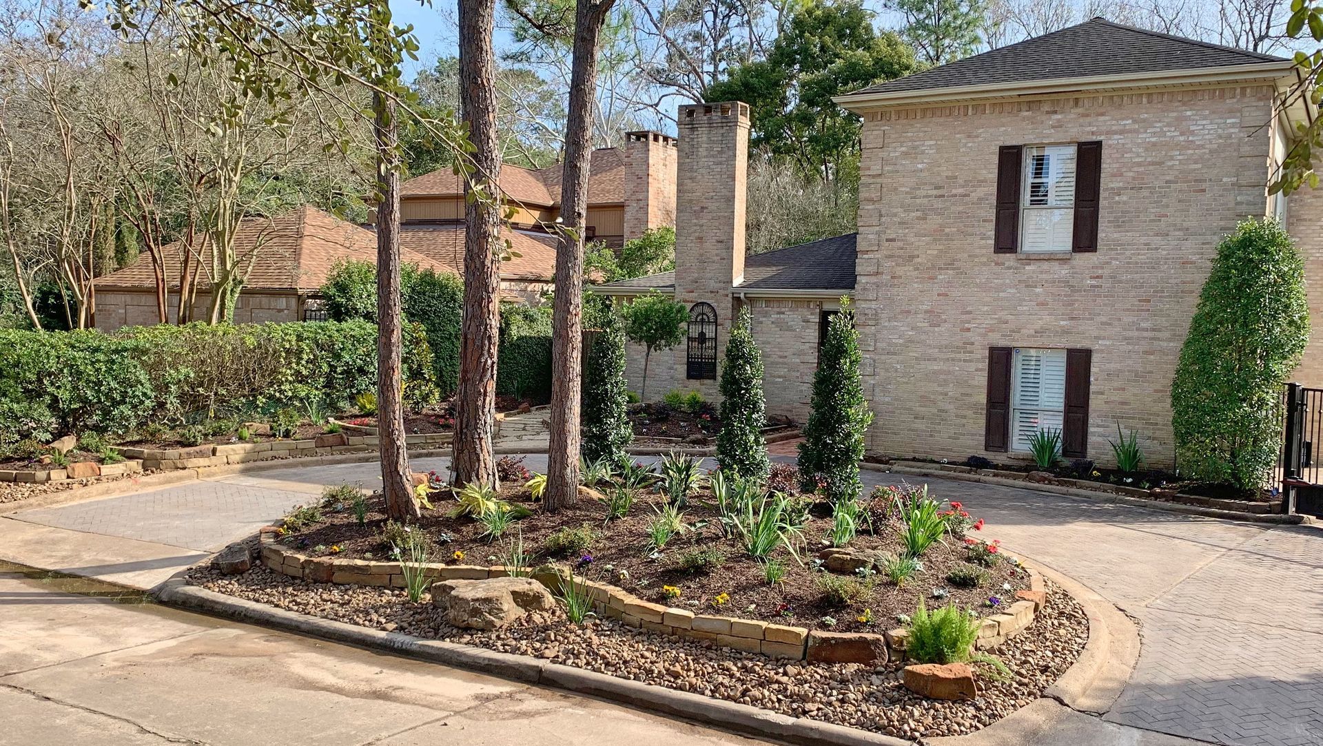 Landscaped courtyard with trees, shrubs, and stone townhouses beside a paved drive