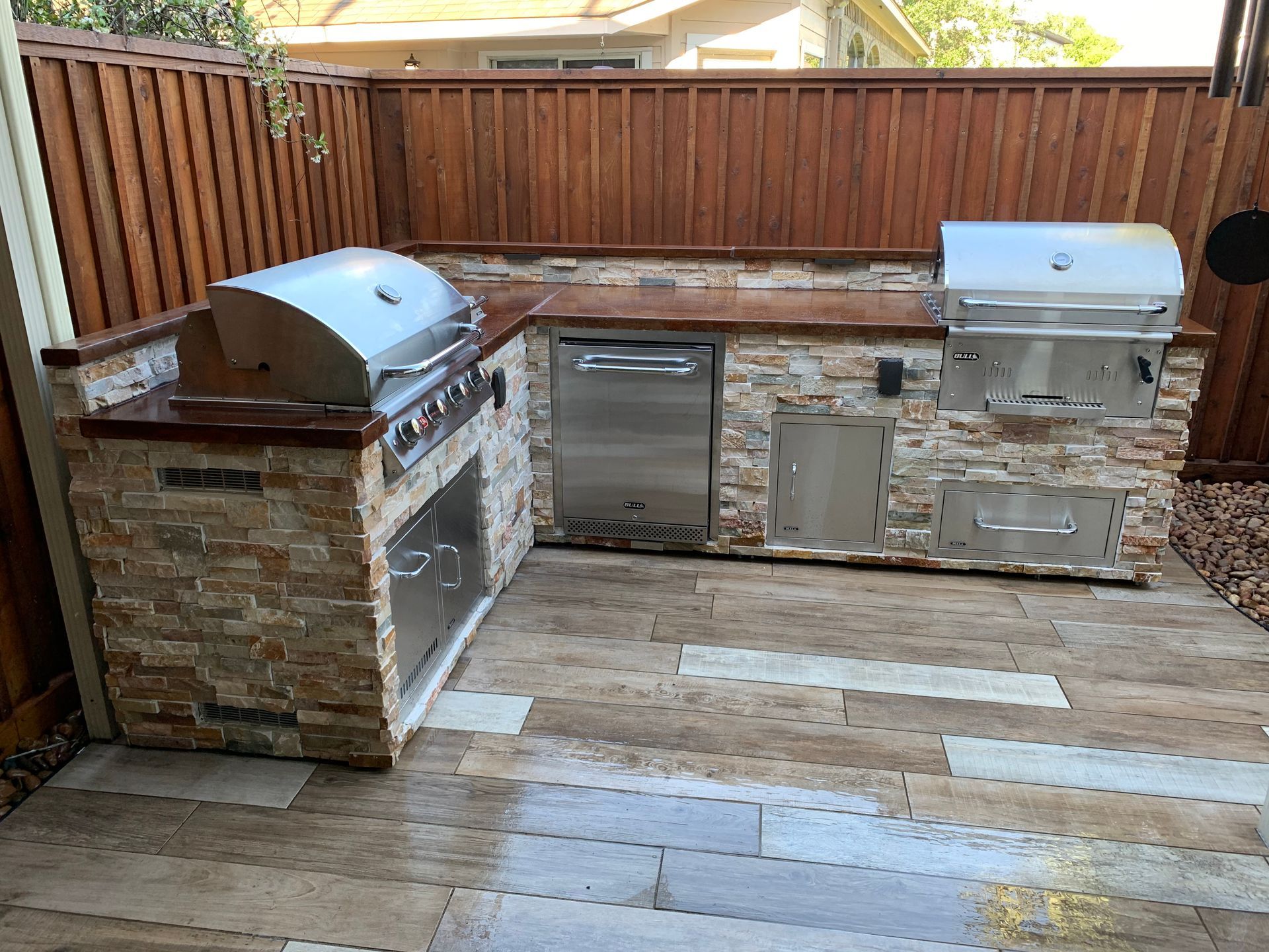 Outdoor patio with stainless steel grill and stone outdoor kitchen along a wooden fence