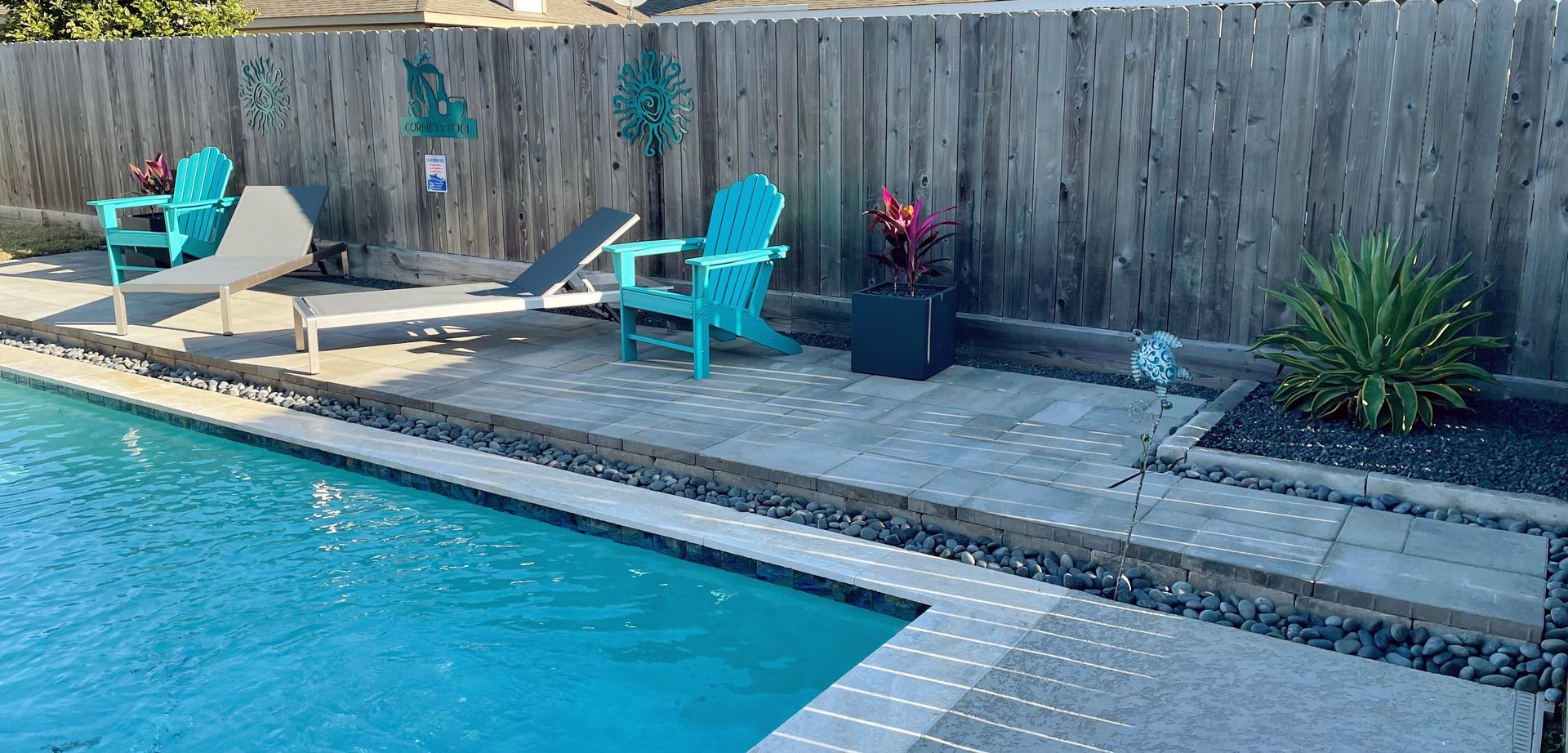 Backyard pool with turquoise lounge chairs, potted plants, and a wooden fence