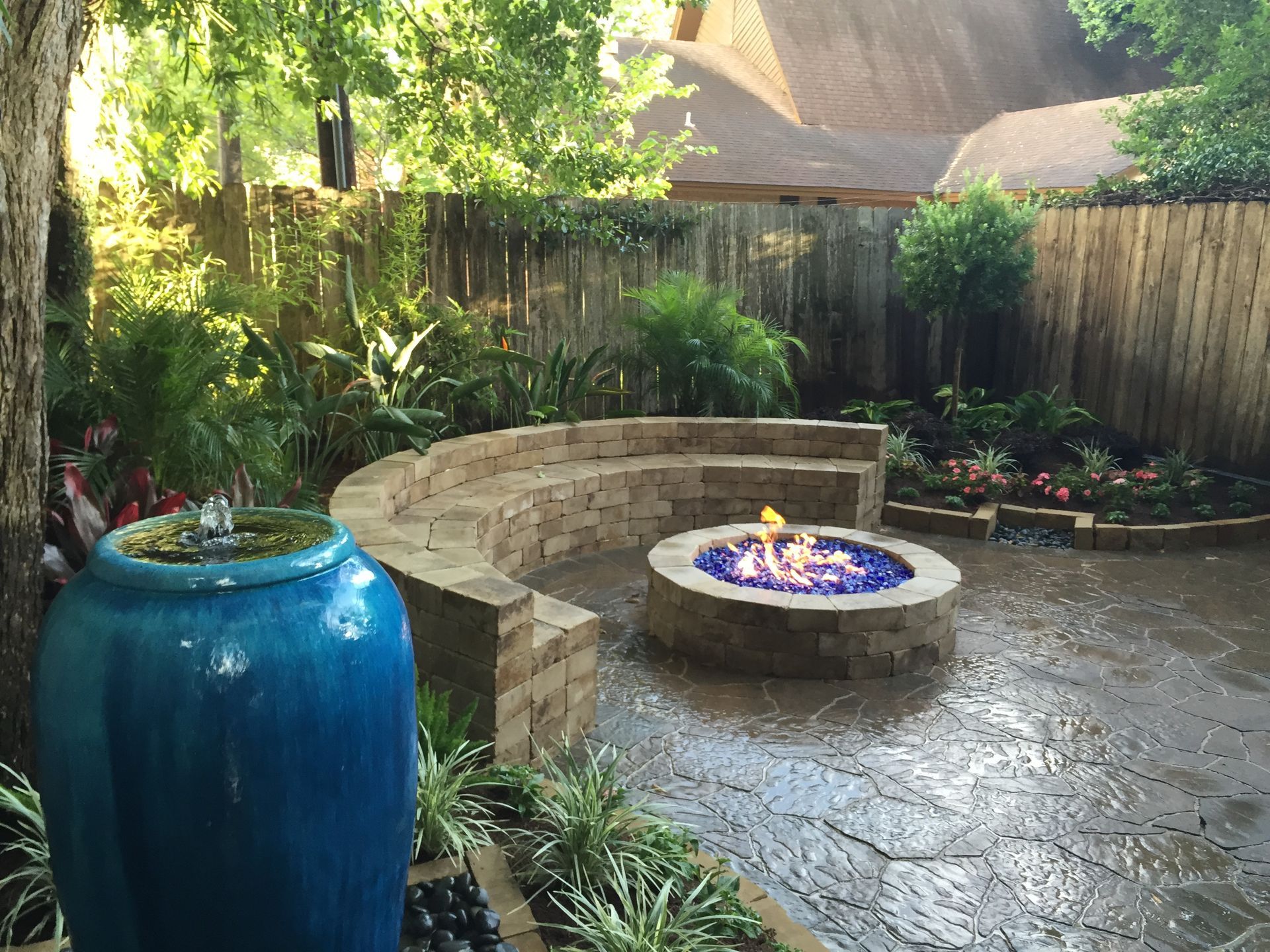 Backyard patio with a blue planter and a stone fire pit surrounded by greenery