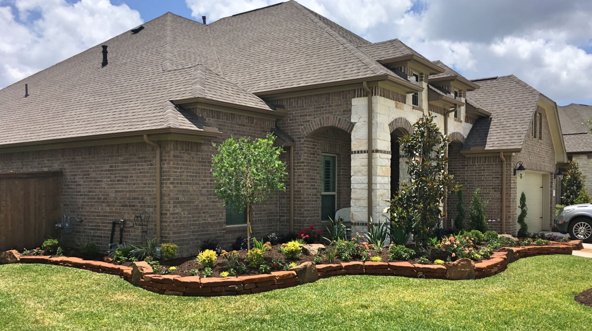 Large suburban brick house with a gray roof, stone entryway, and landscaped front yard