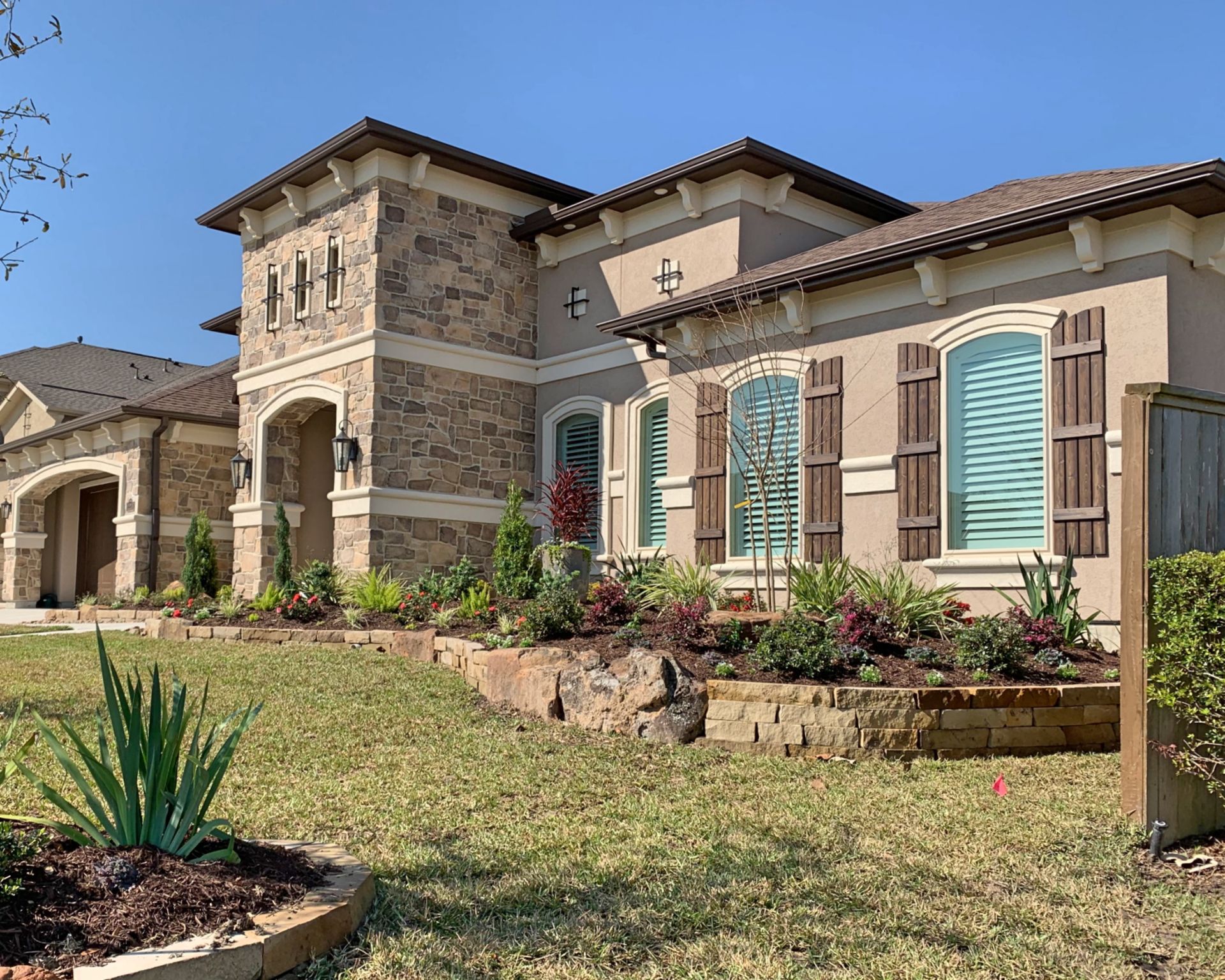 Suburban Mediterranean-style house with stone tower, tan stucco walls, and blue shutters under a clear sky