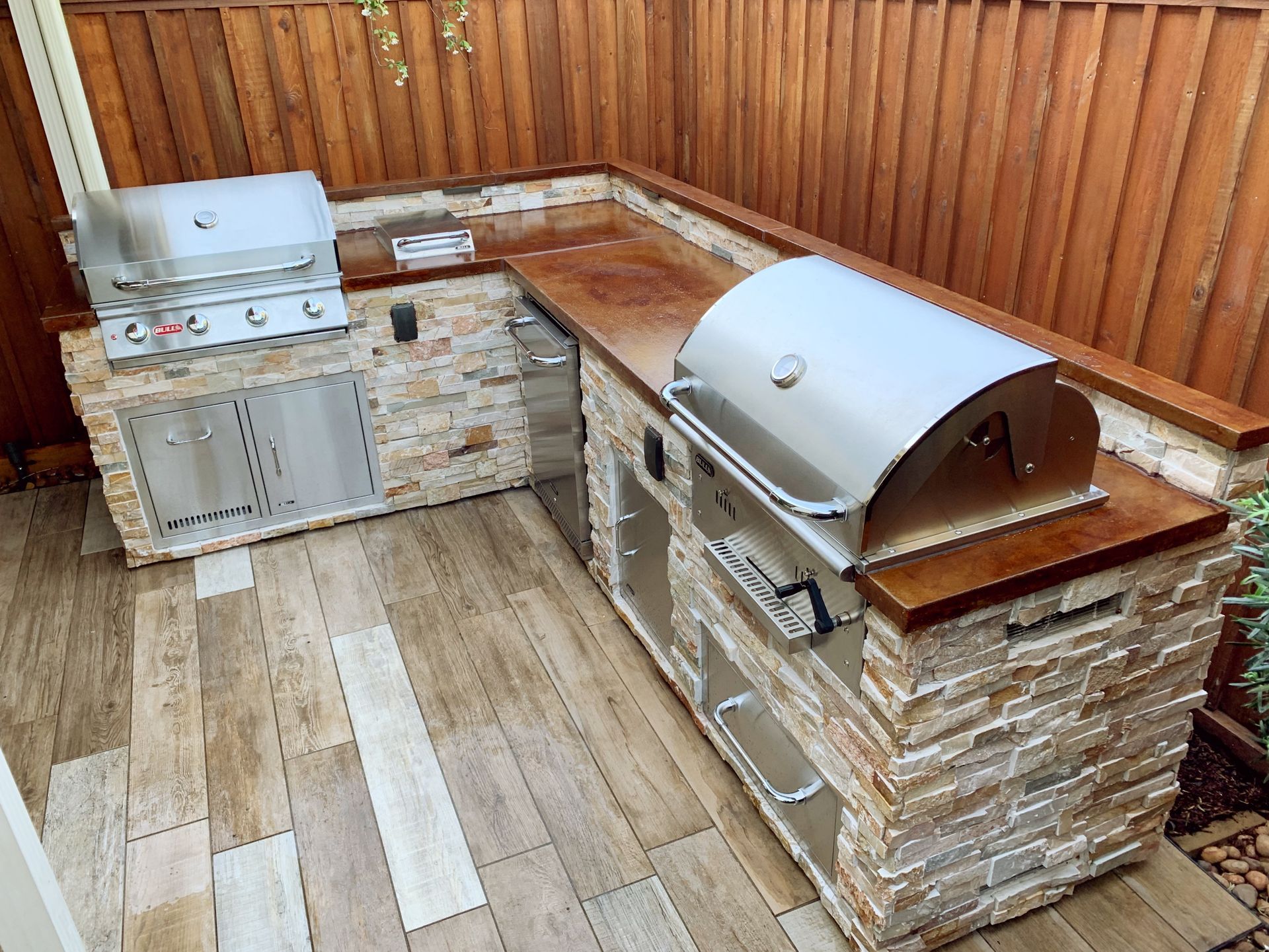 Outdoor patio with built-in stone grill and countertop against a wooden fence