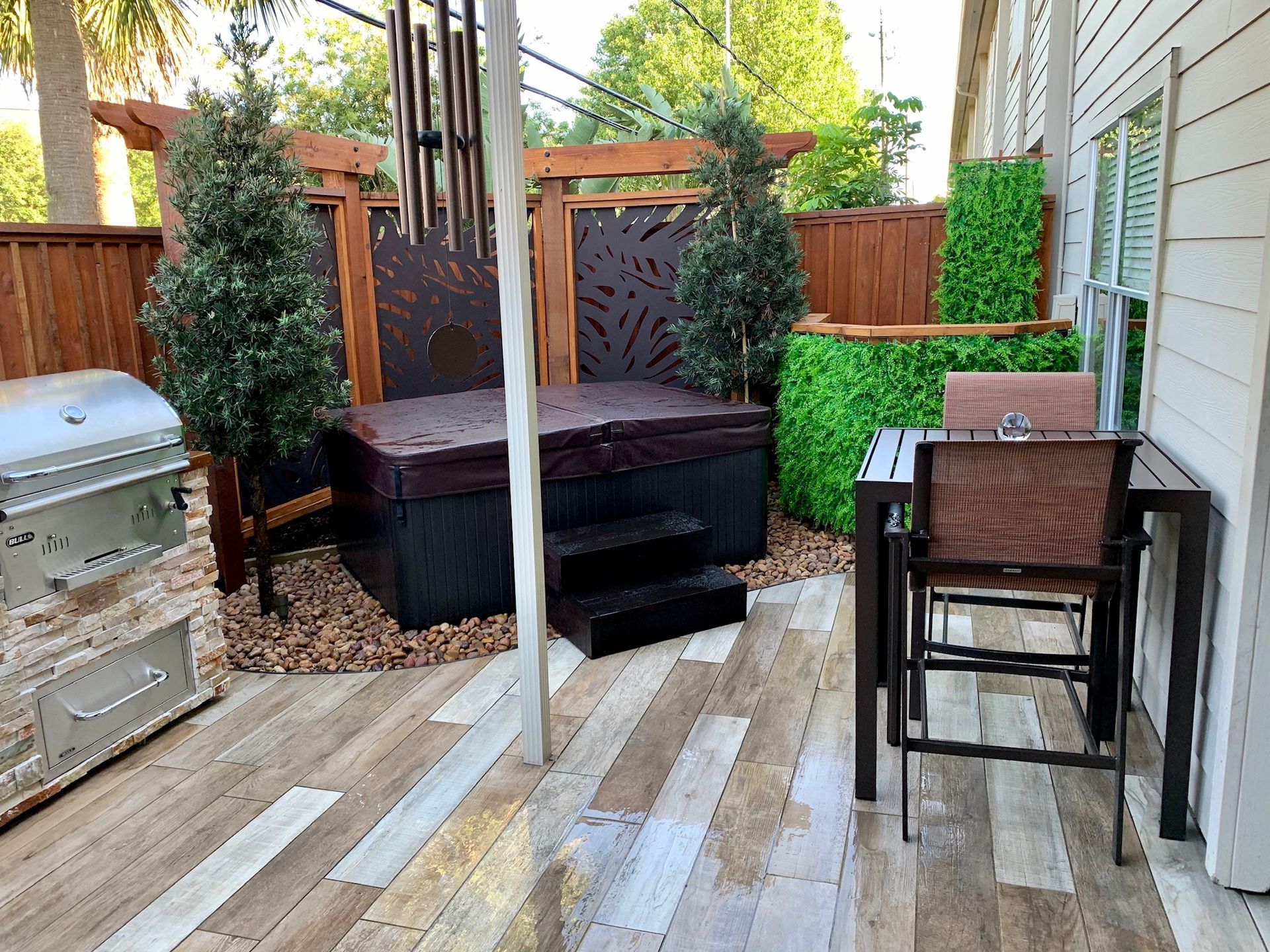 Small backyard patio with hot tub, grill, table, chairs, and fenced seating area