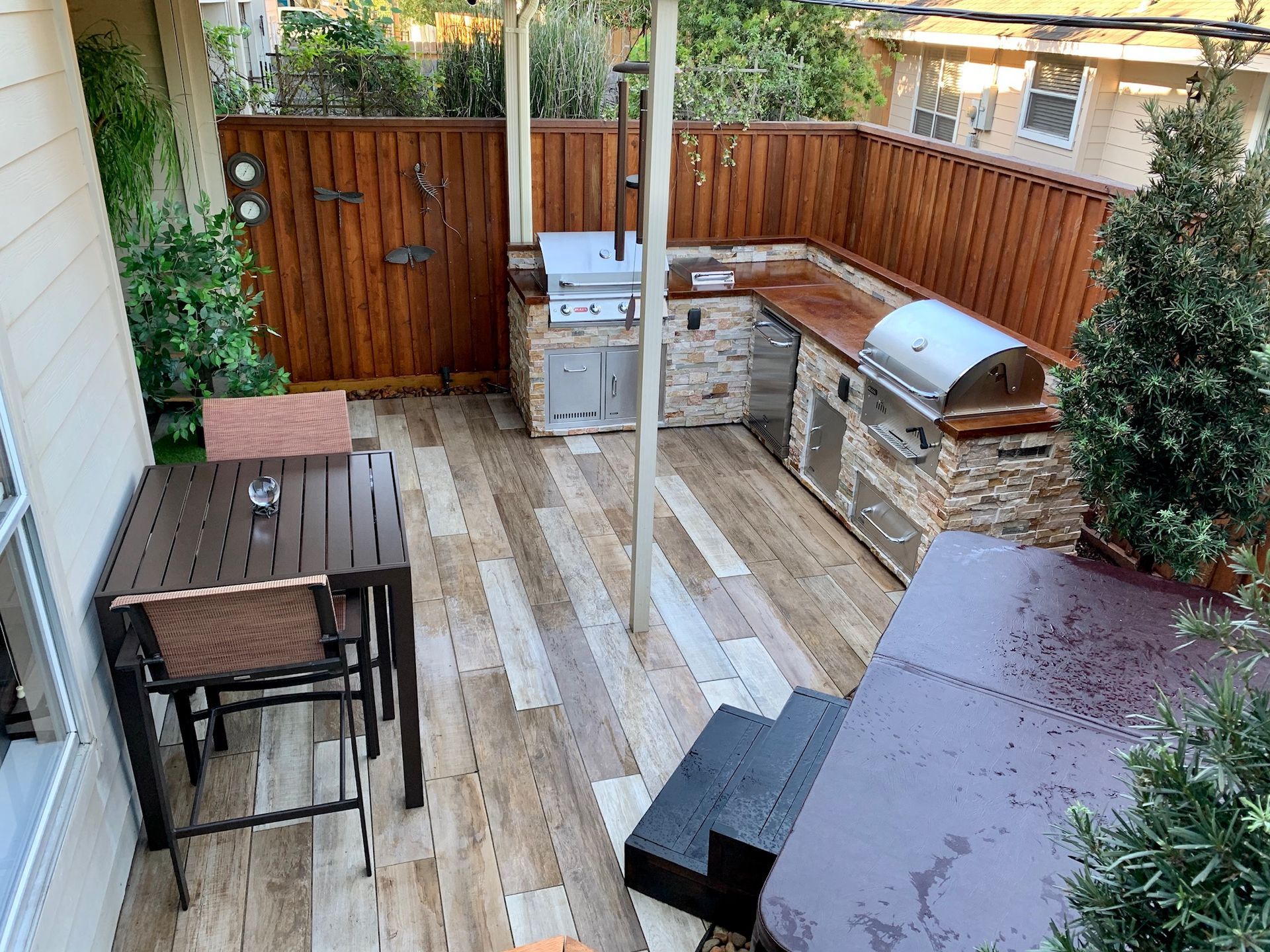 Backyard patio with wooden deck, outdoor dining set, storage boxes, grill, and potted shrubs