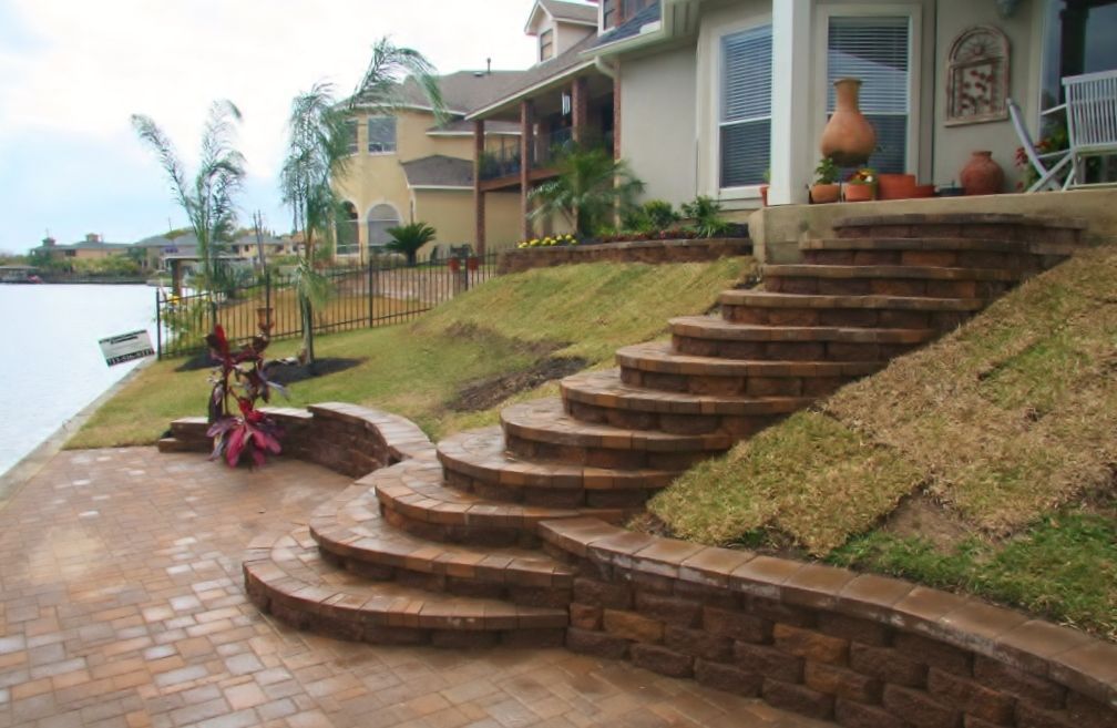 Curved brick steps beside a lakeside house with a paved patio and lawn
