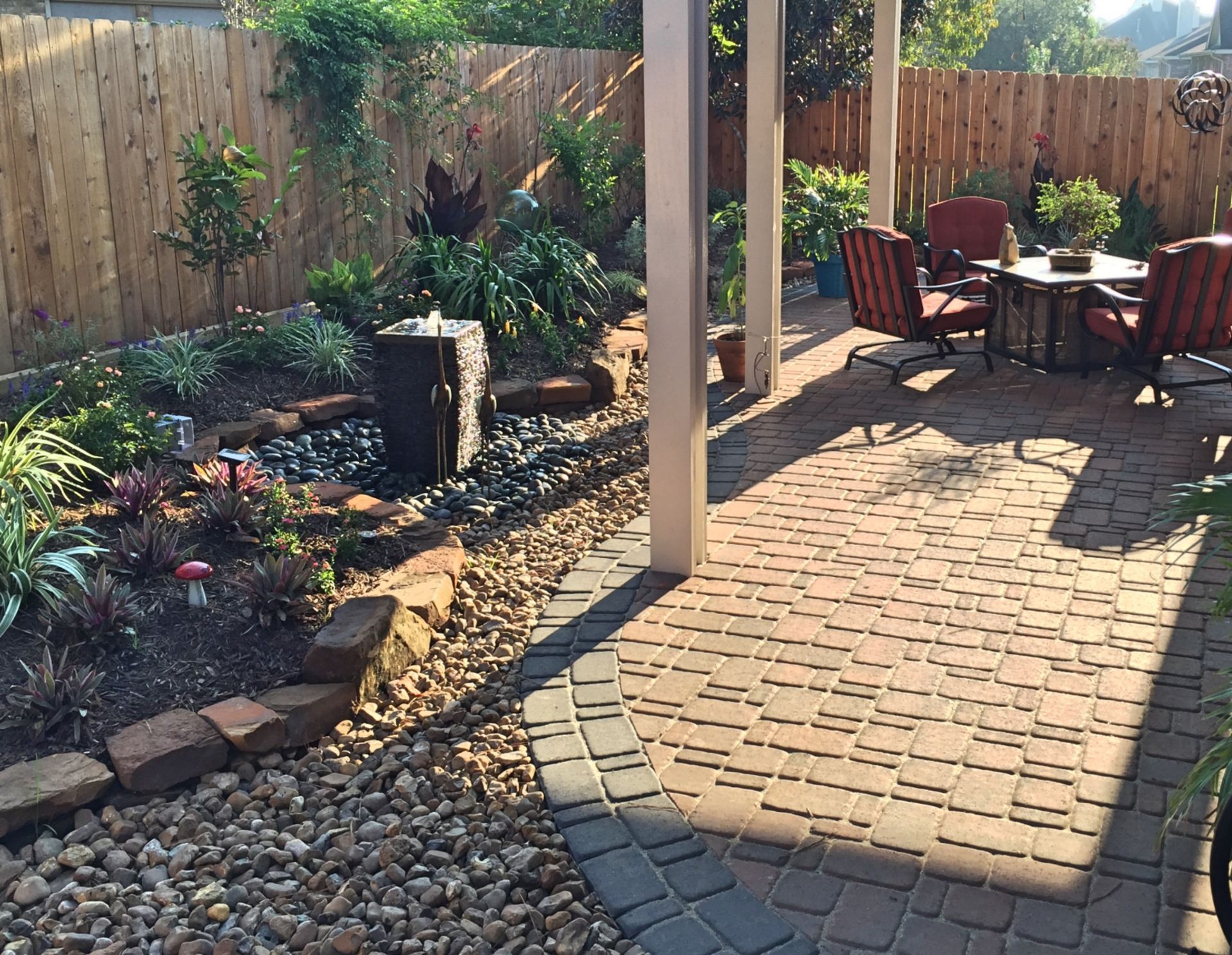 Covered patio with brick pavers, rock garden, and outdoor seating by a wooden fence