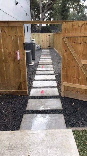 Open wooden gate leading to a narrow stone path through a fenced yard.