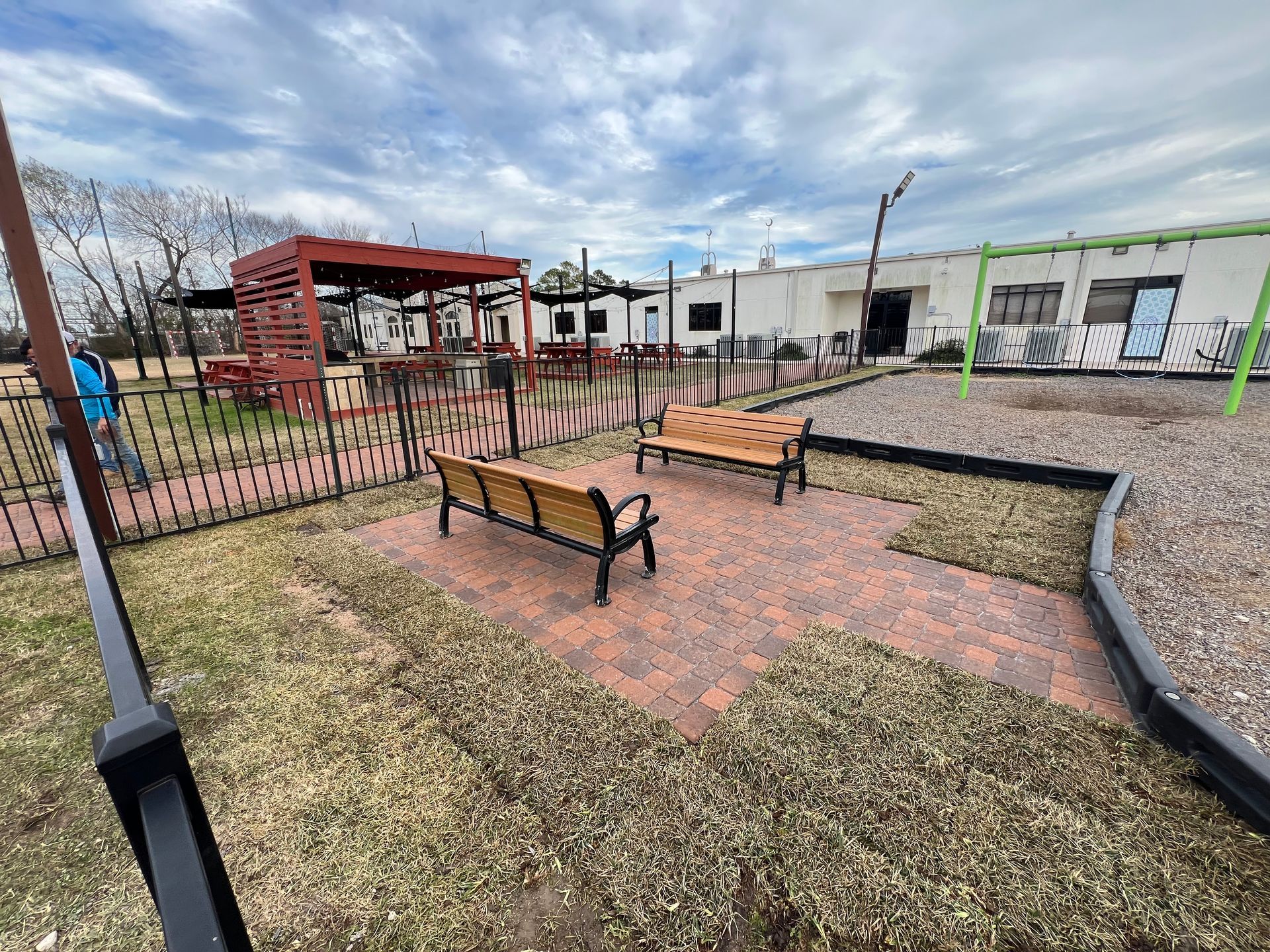 Outdoor seating area with two wooden benches on a brick patio in a fenced yard.