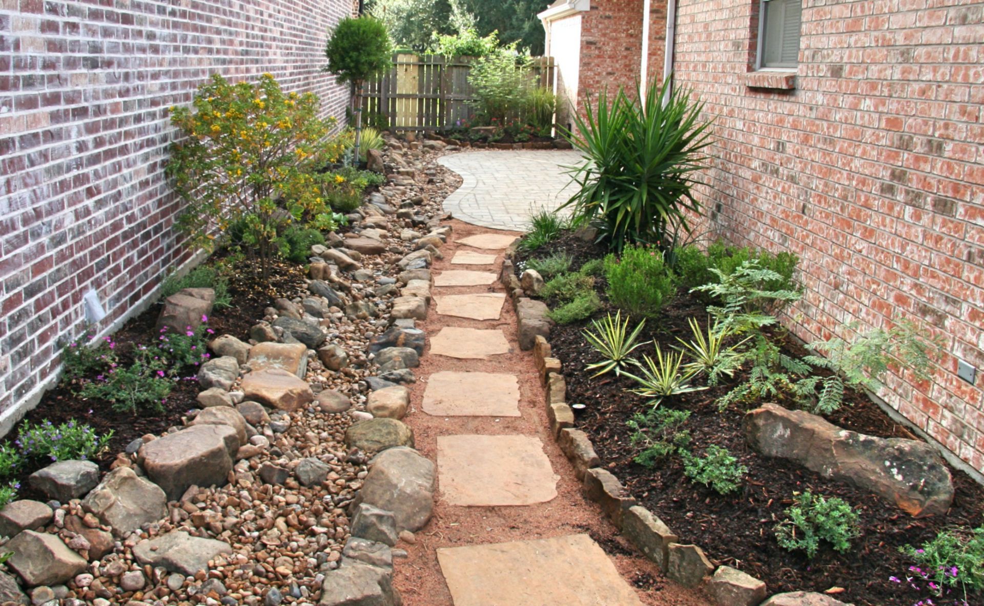 Narrow stone path through a landscaped garden between two brick walls