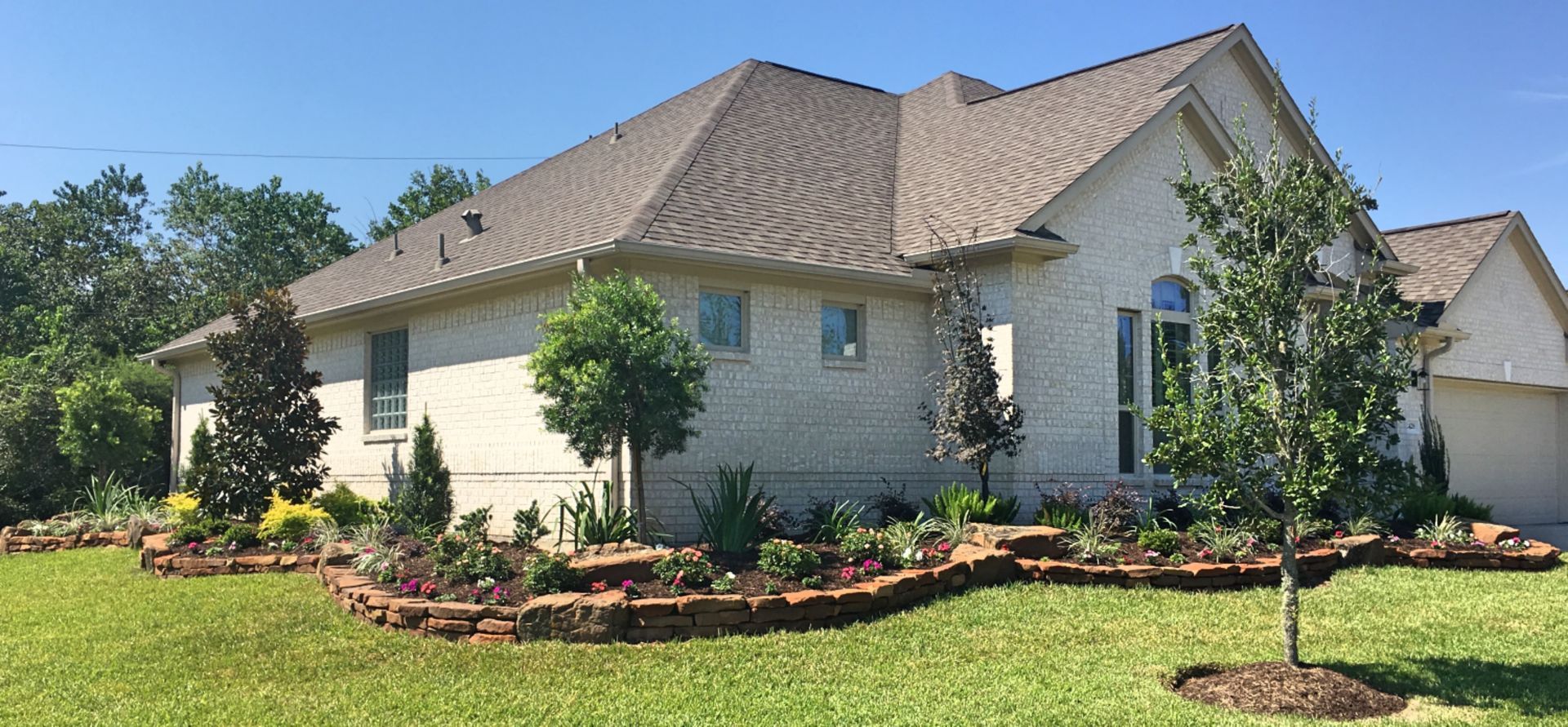 Single-story beige house with a brown roof and landscaped front yard under a blue sky