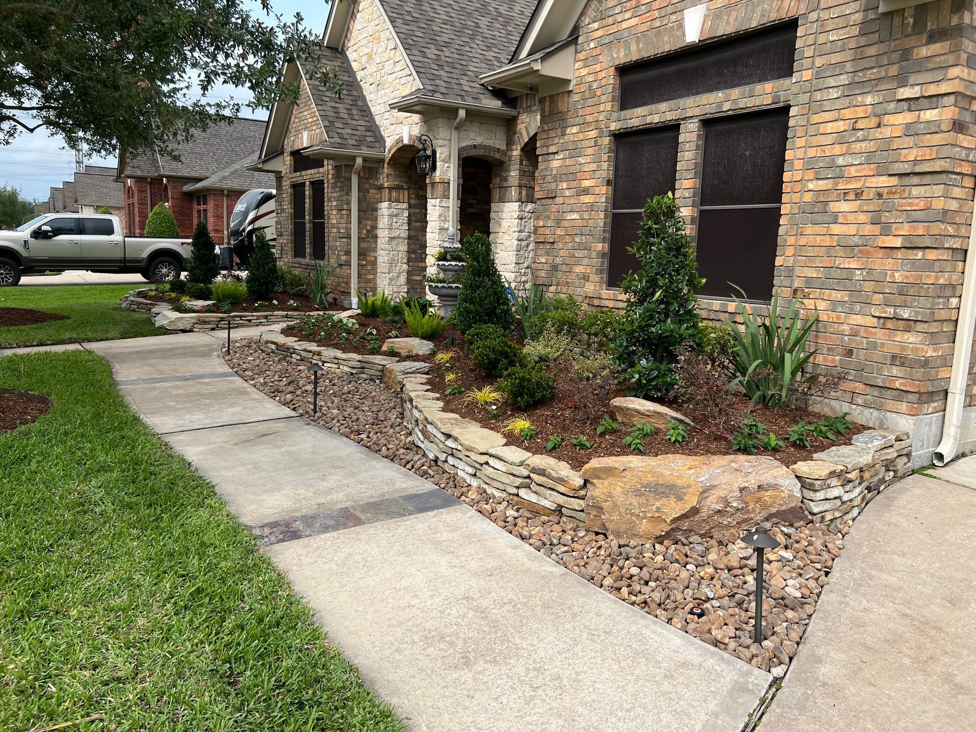 Front walkway and landscaped flower bed beside a brick house with stone accents