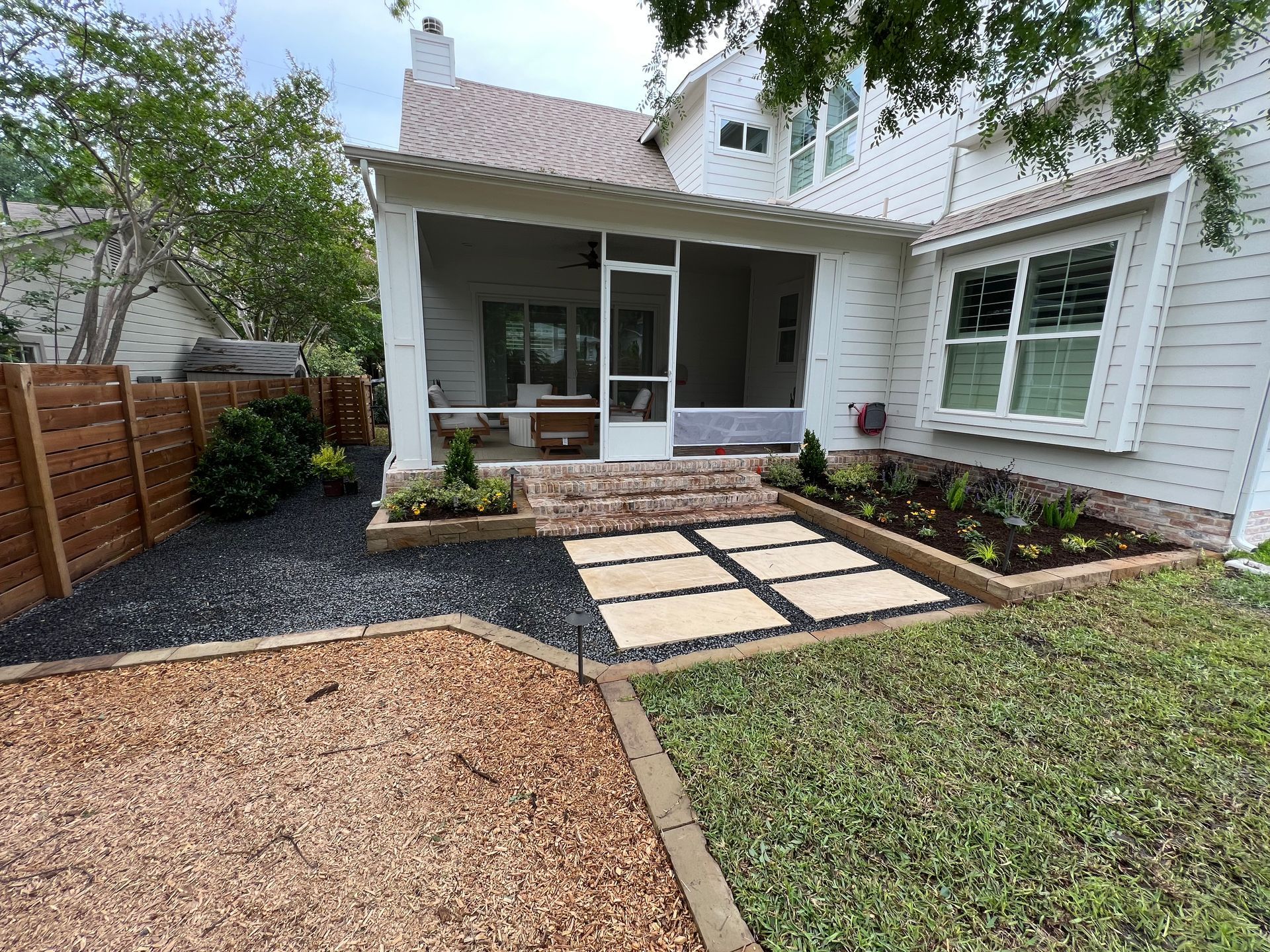 Front patio with pavers, mulch, and lawn beside a white house and covered porch