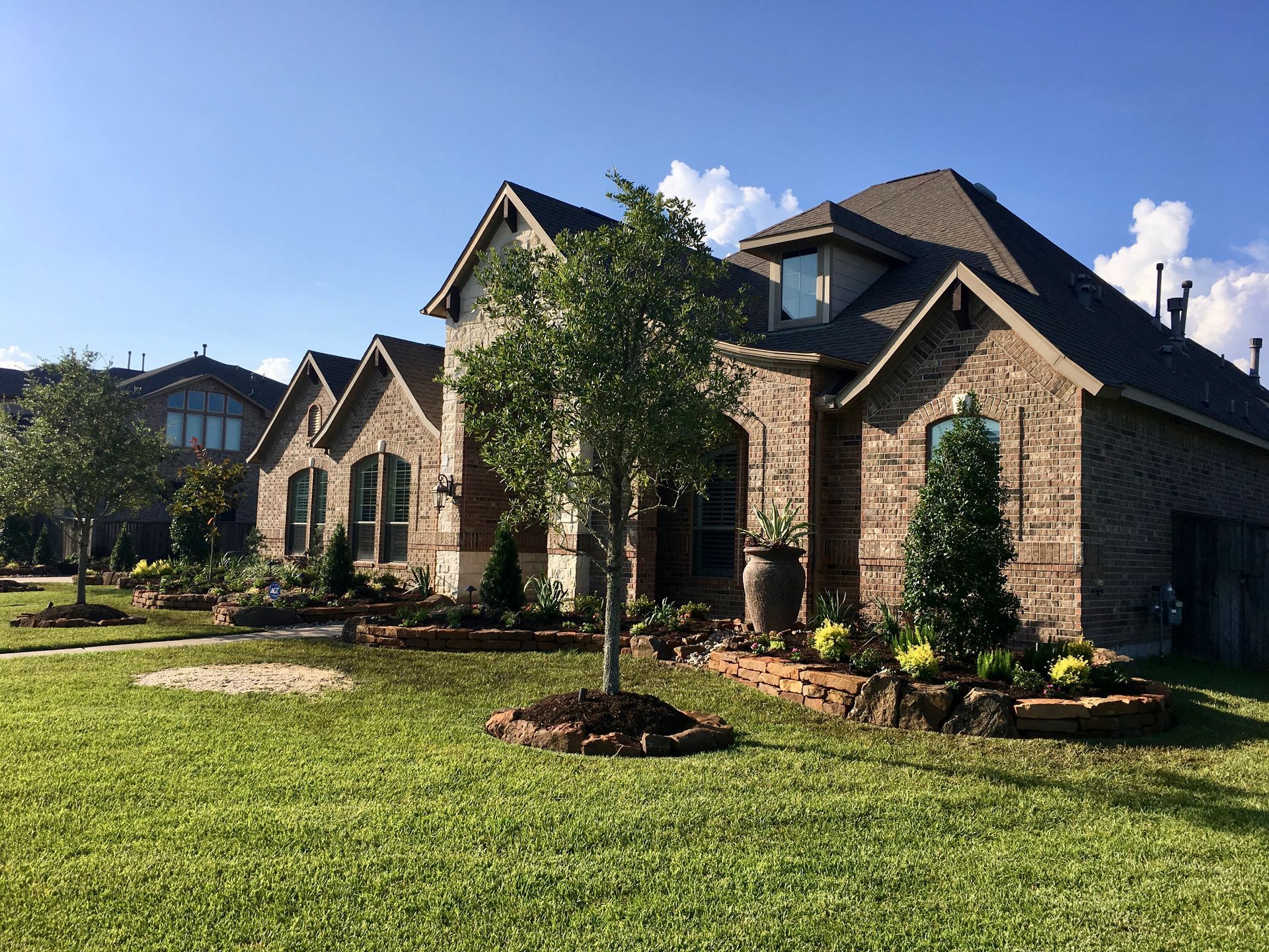 Suburban brick house with stone accents, green lawn, and landscaped front yard under a blue sky