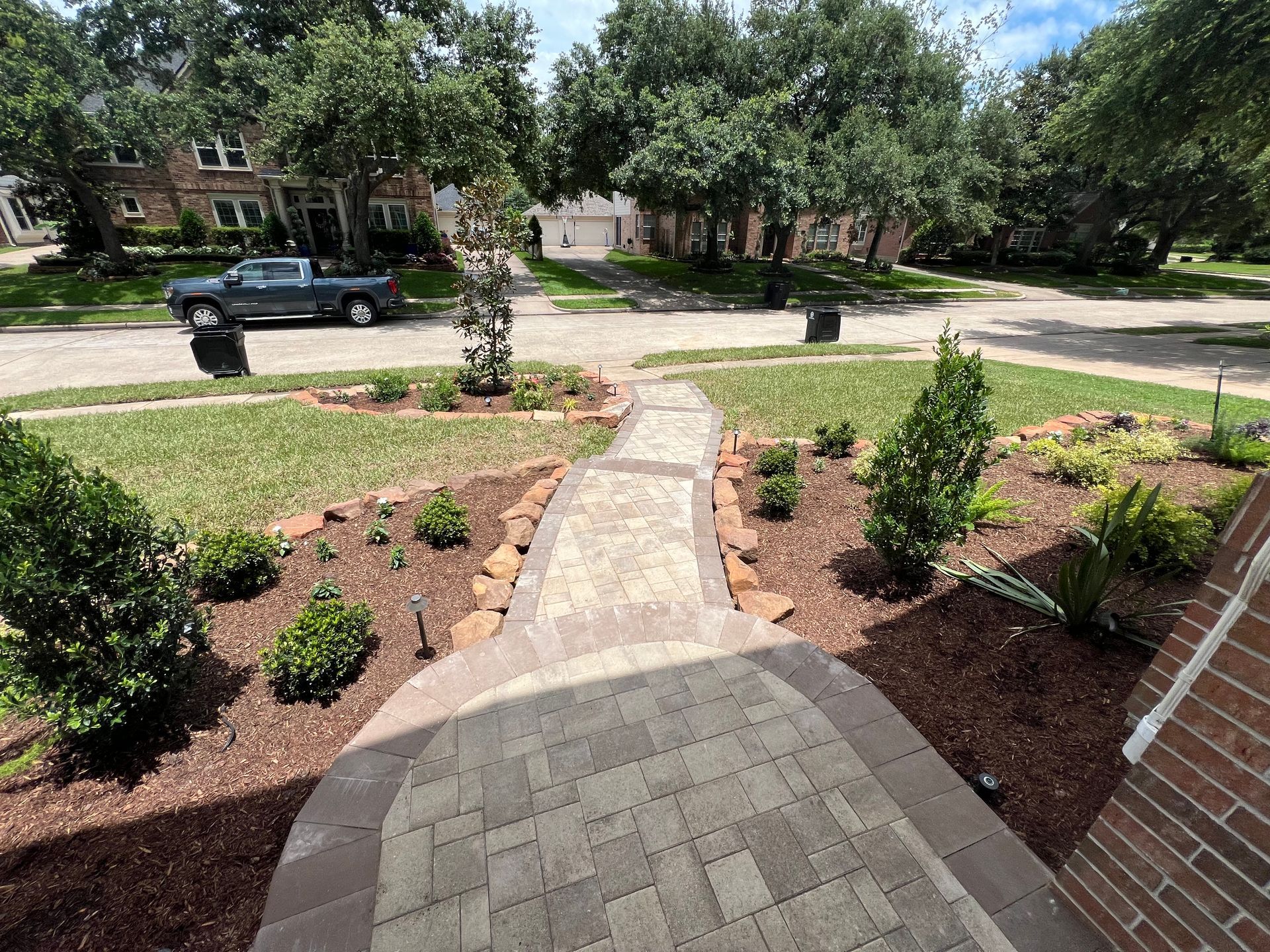 Front porch walkway leading to a landscaped front yard and tree-lined suburban street