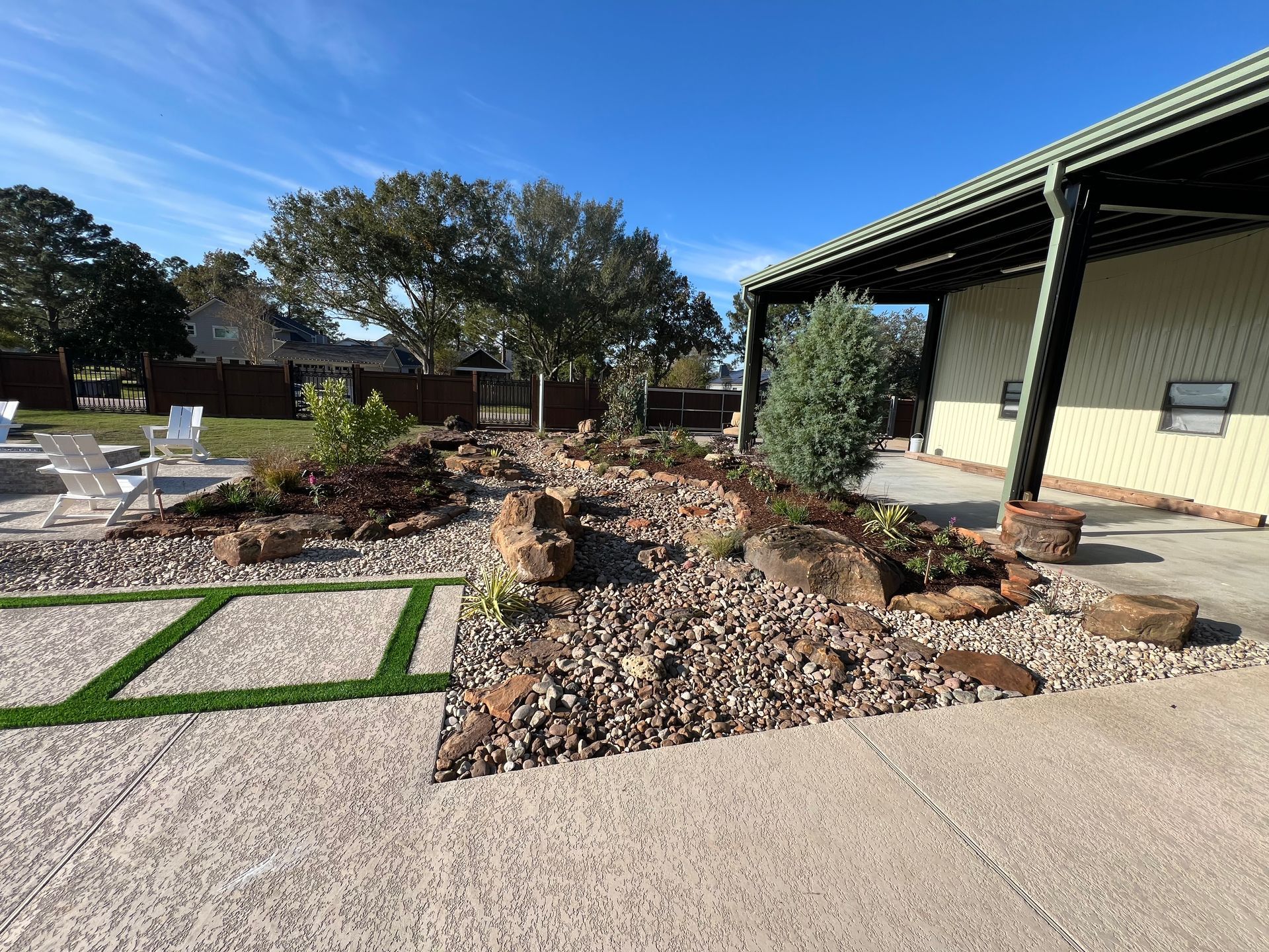 Outdoor patio with rock garden, raised flower beds, and white chairs beside a building