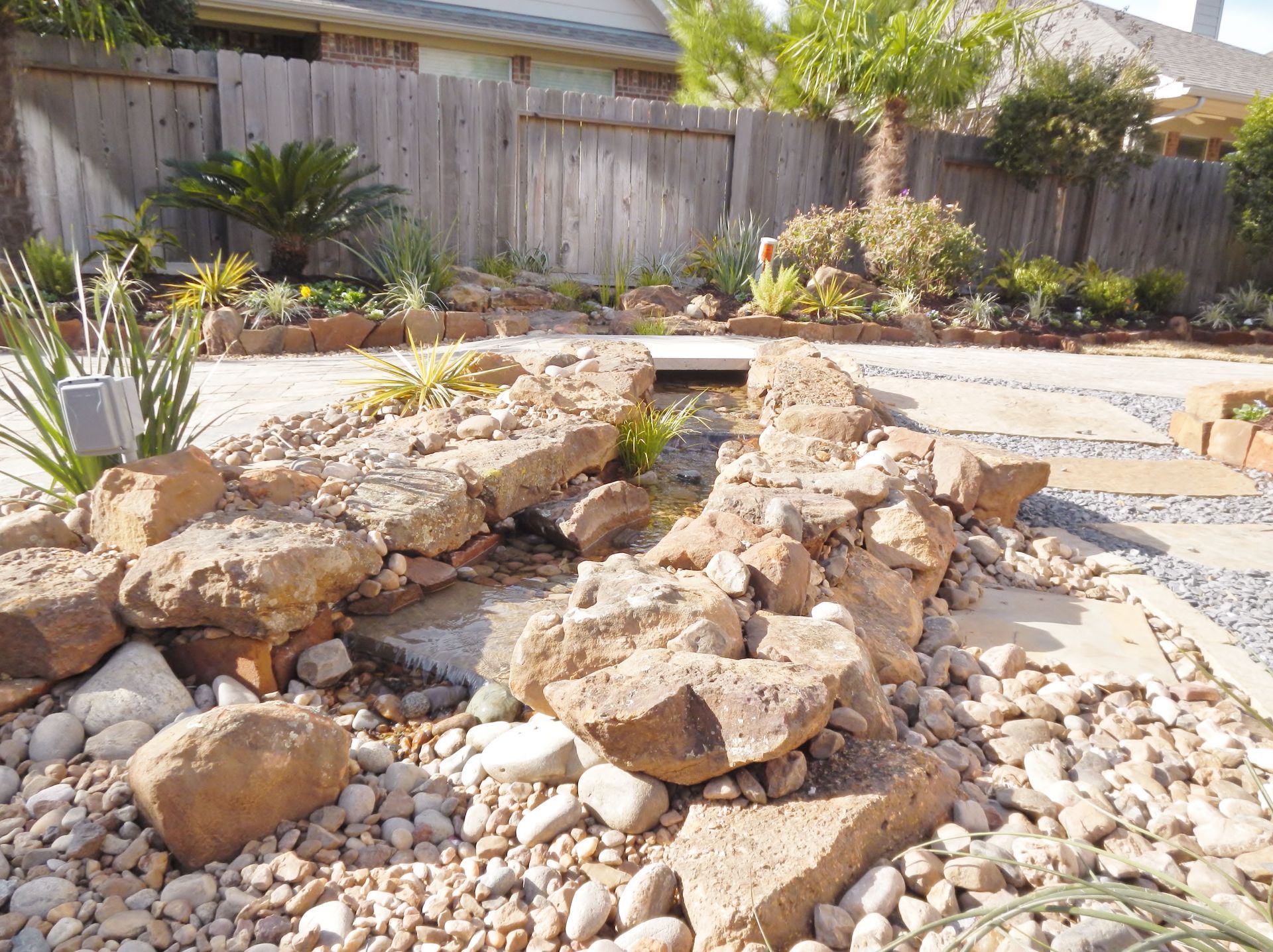 Rock garden with large tan stones, gravel, and desert plants in a fenced backyard.