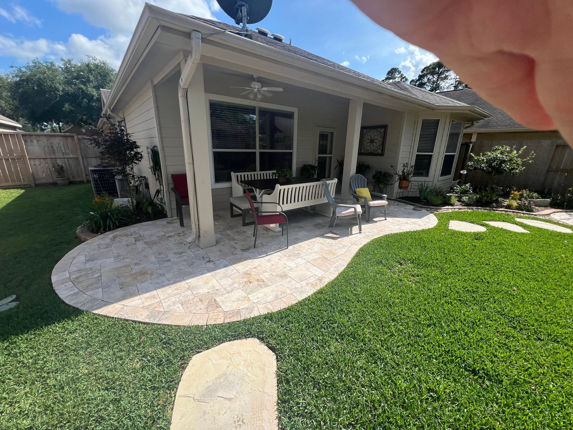 Backyard patio with white house, bench, potted plants, and curved stone walkway overlooking green lawn