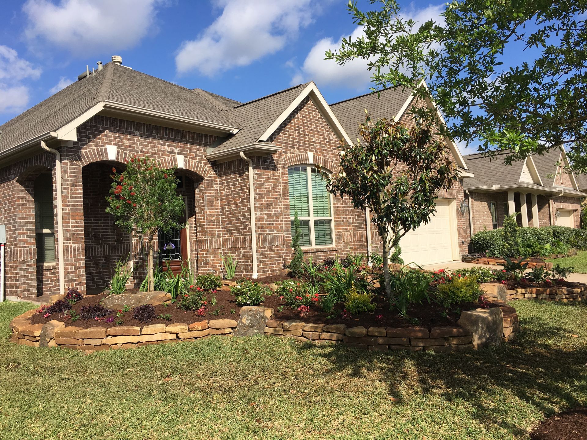 Brick suburban house with arched front porch, landscaped yard, and blue sky overhead