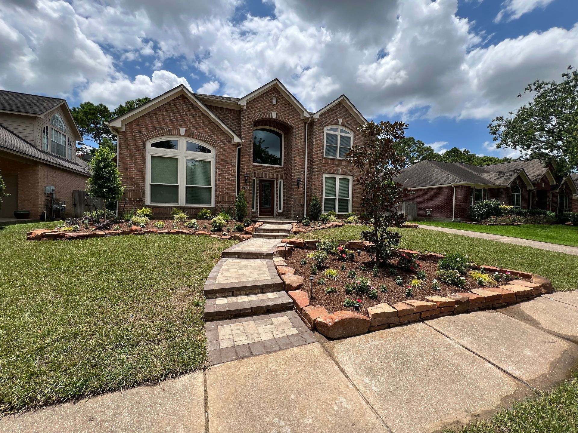 Brick suburban house with landscaped front yard, stone walkway, and cloudy sky