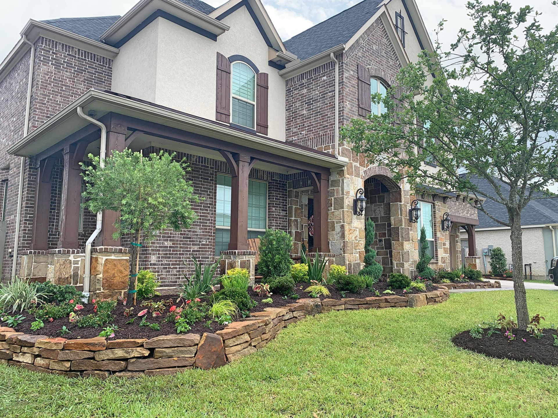 Two-story brick house with stone accents, landscaped garden, and a green lawn in front