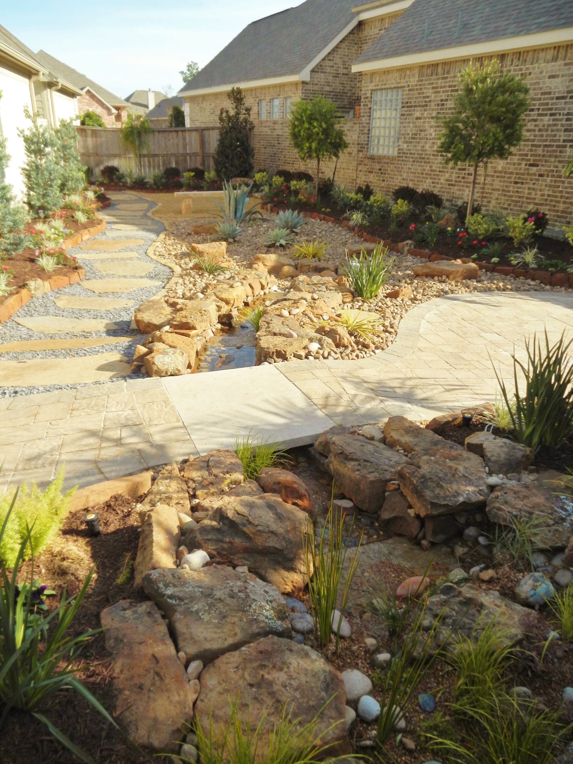 Desert-style front yard with stone paths, rock garden, and brick houses in warm sunlight