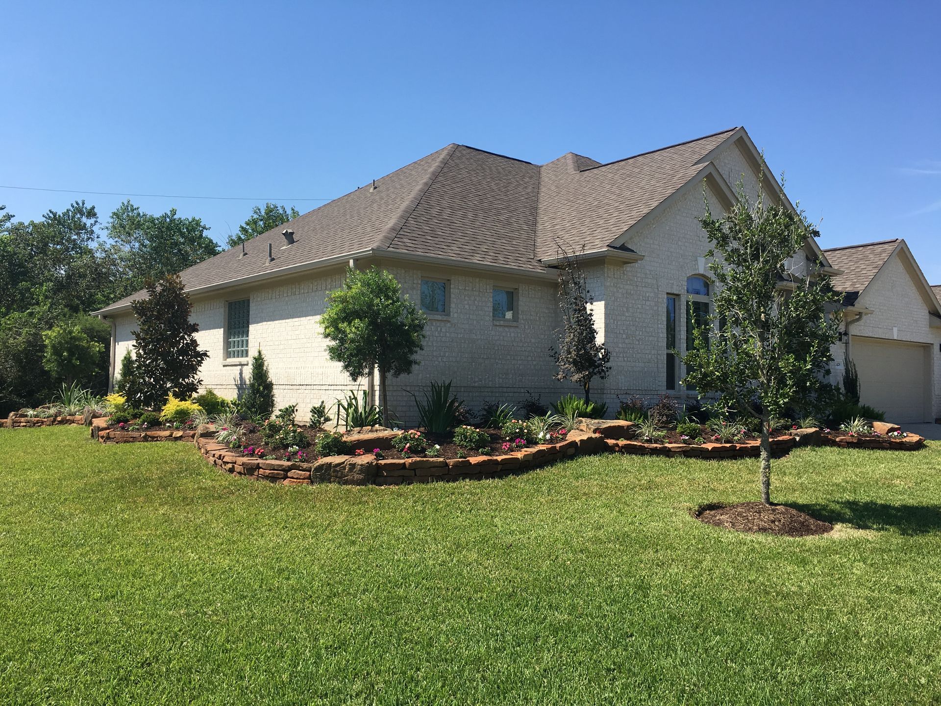 Single-story beige house with tan roof and landscaped front yard under a blue sky