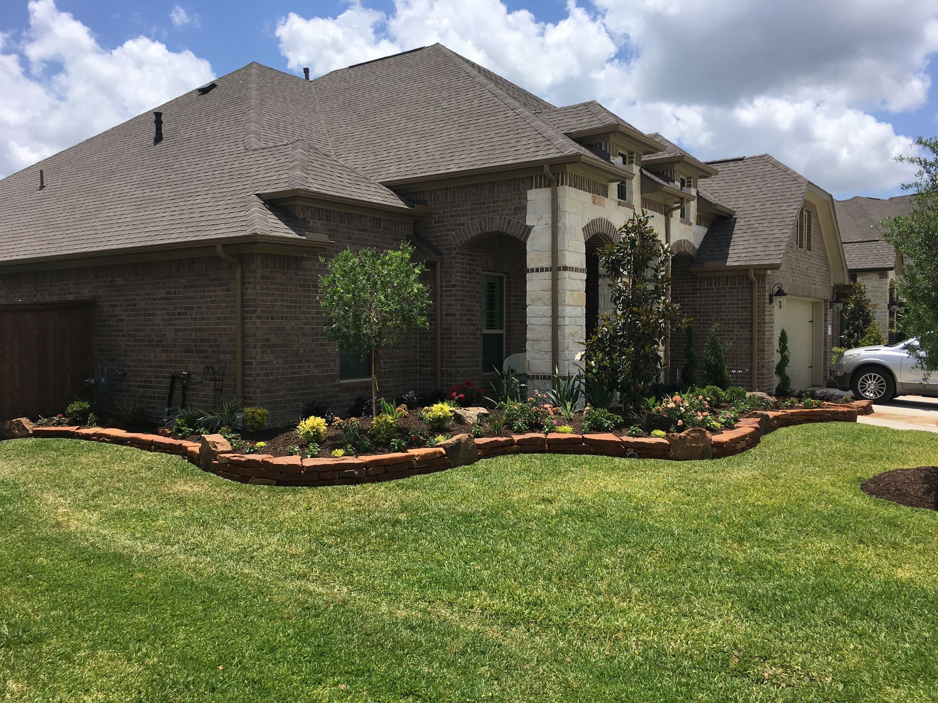 Brick suburban house with a manicured lawn, flower beds, and a cloudy sky