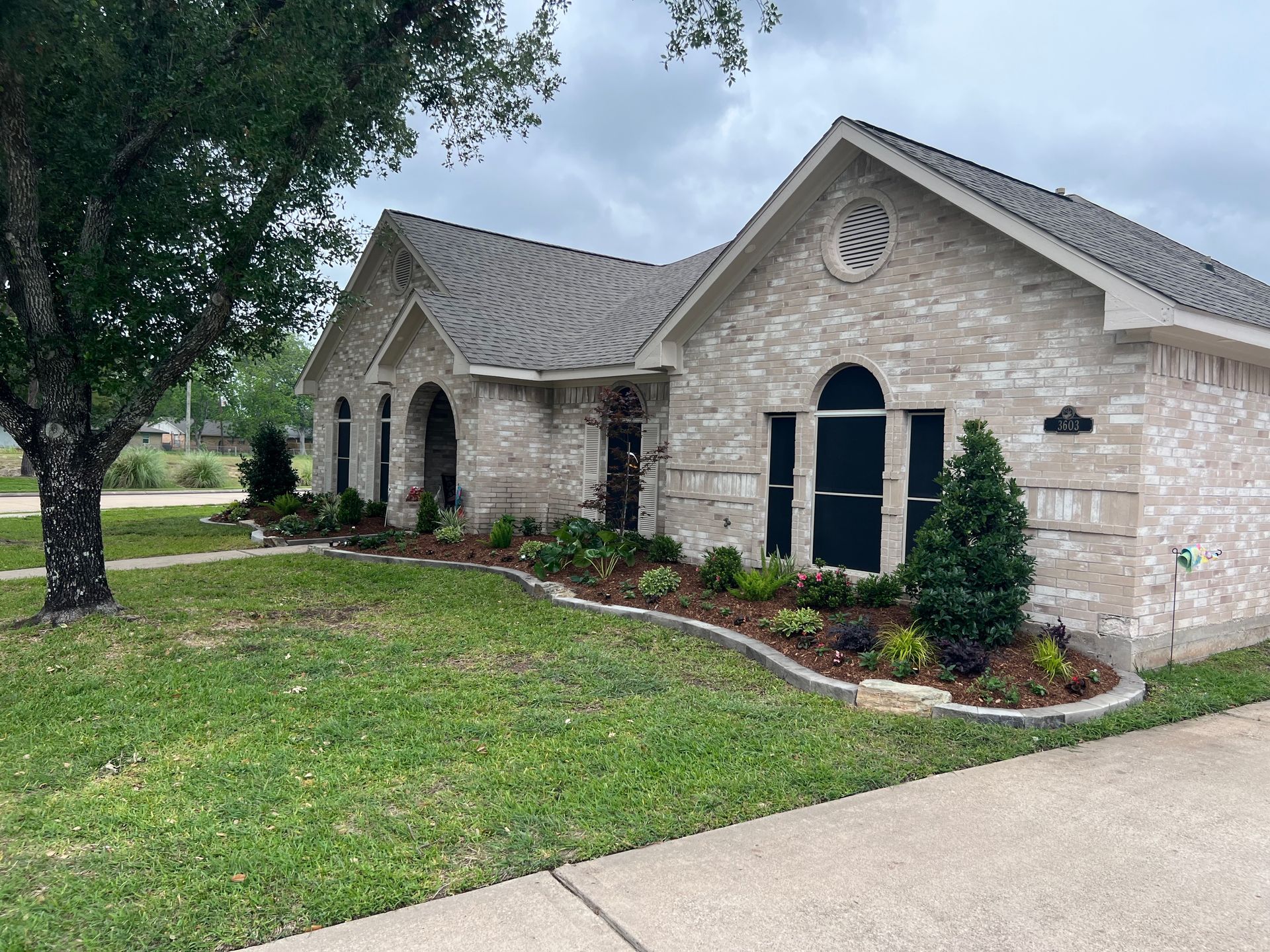 Single-story stone house with arched windows, a front lawn, and a large tree in the yard.
