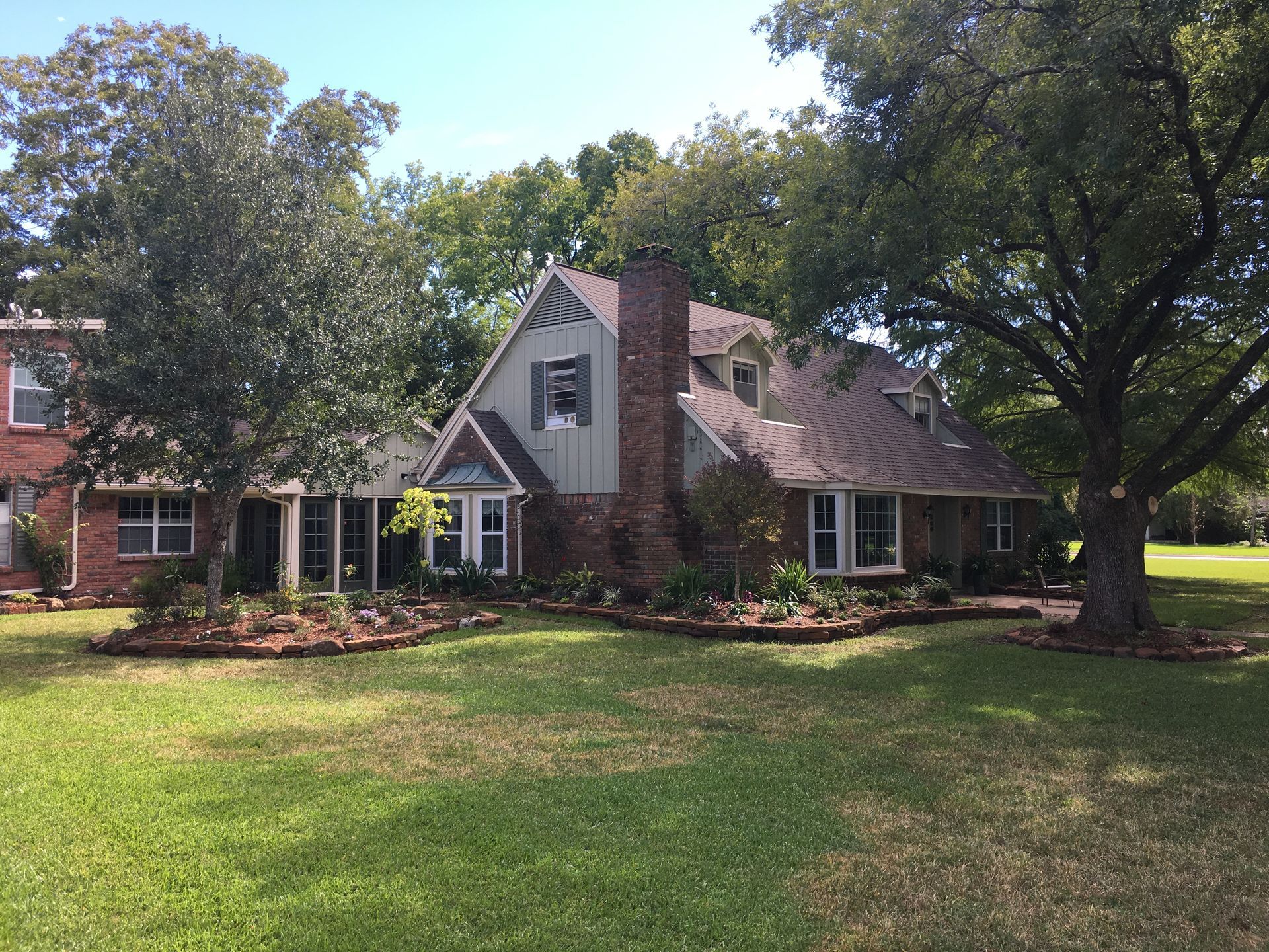 Suburban brick house with large green lawn and mature trees in front yard