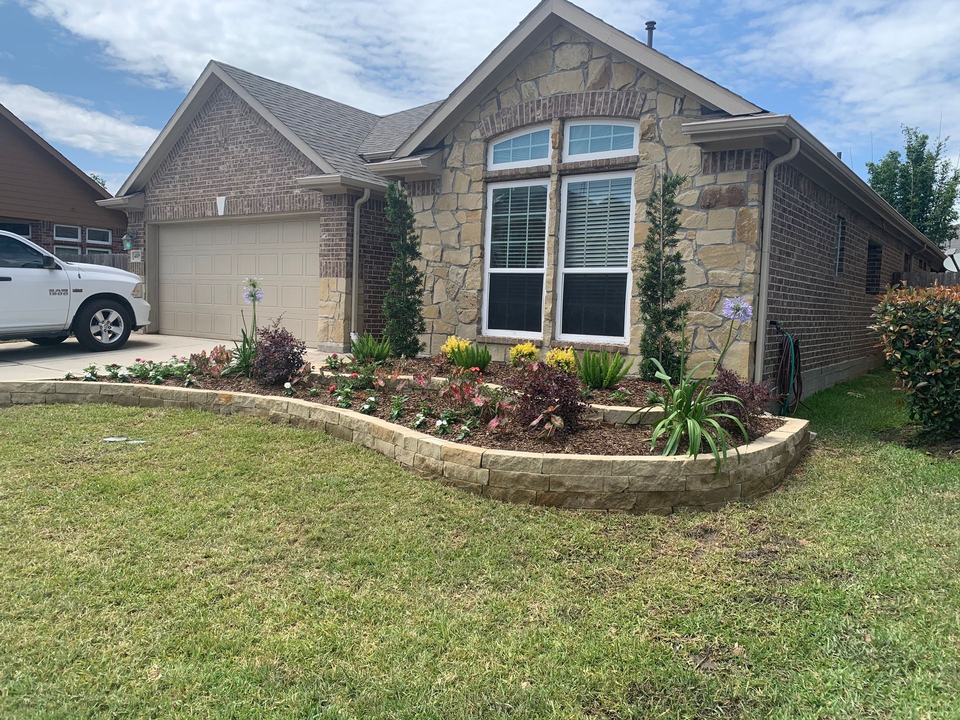 Suburban brick house with a landscaped front yard, large windows, and a parked car in the driveway.