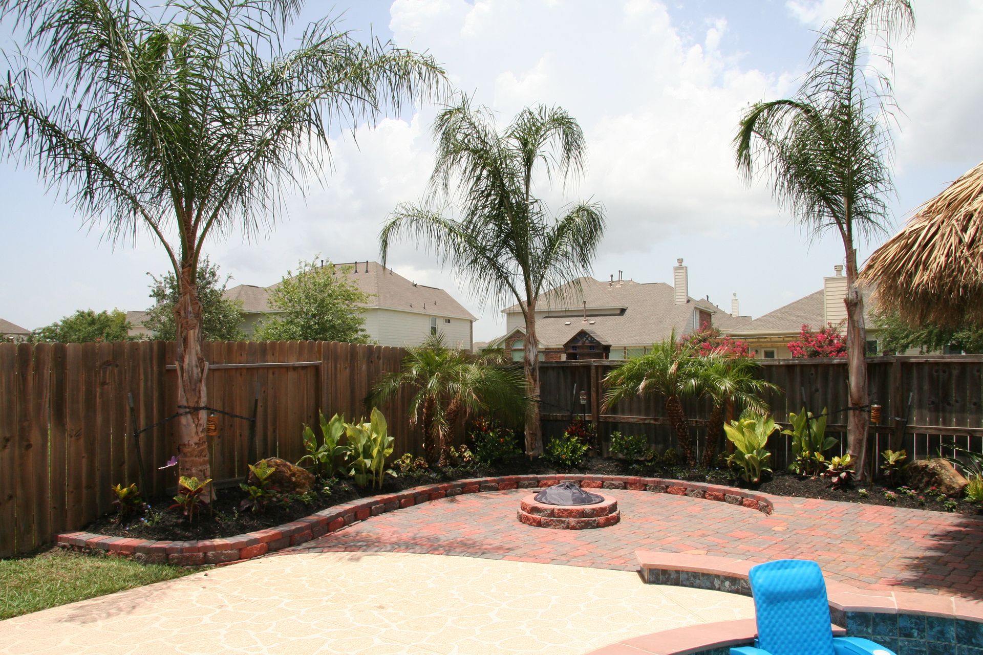 Backyard patio with palm trees, flower beds, and a small pool under a sunny sky