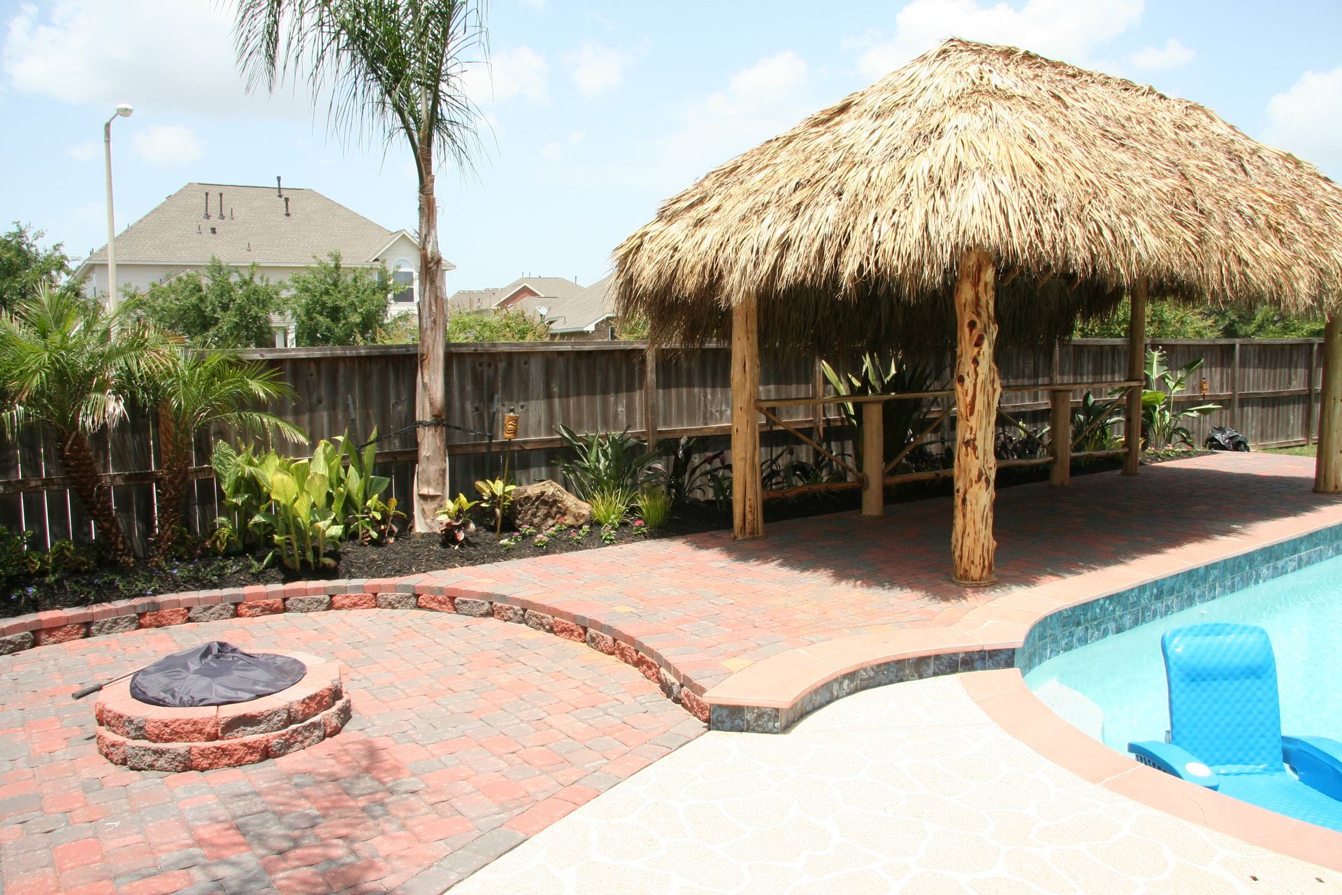 Backyard patio with thatched tiki hut, fire pit, and blue swimming pool under a clear sky