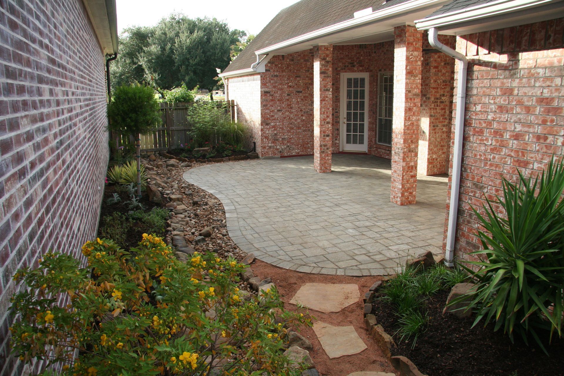 Brick house patio with a curved stone walkway, garden beds, and a screened porch