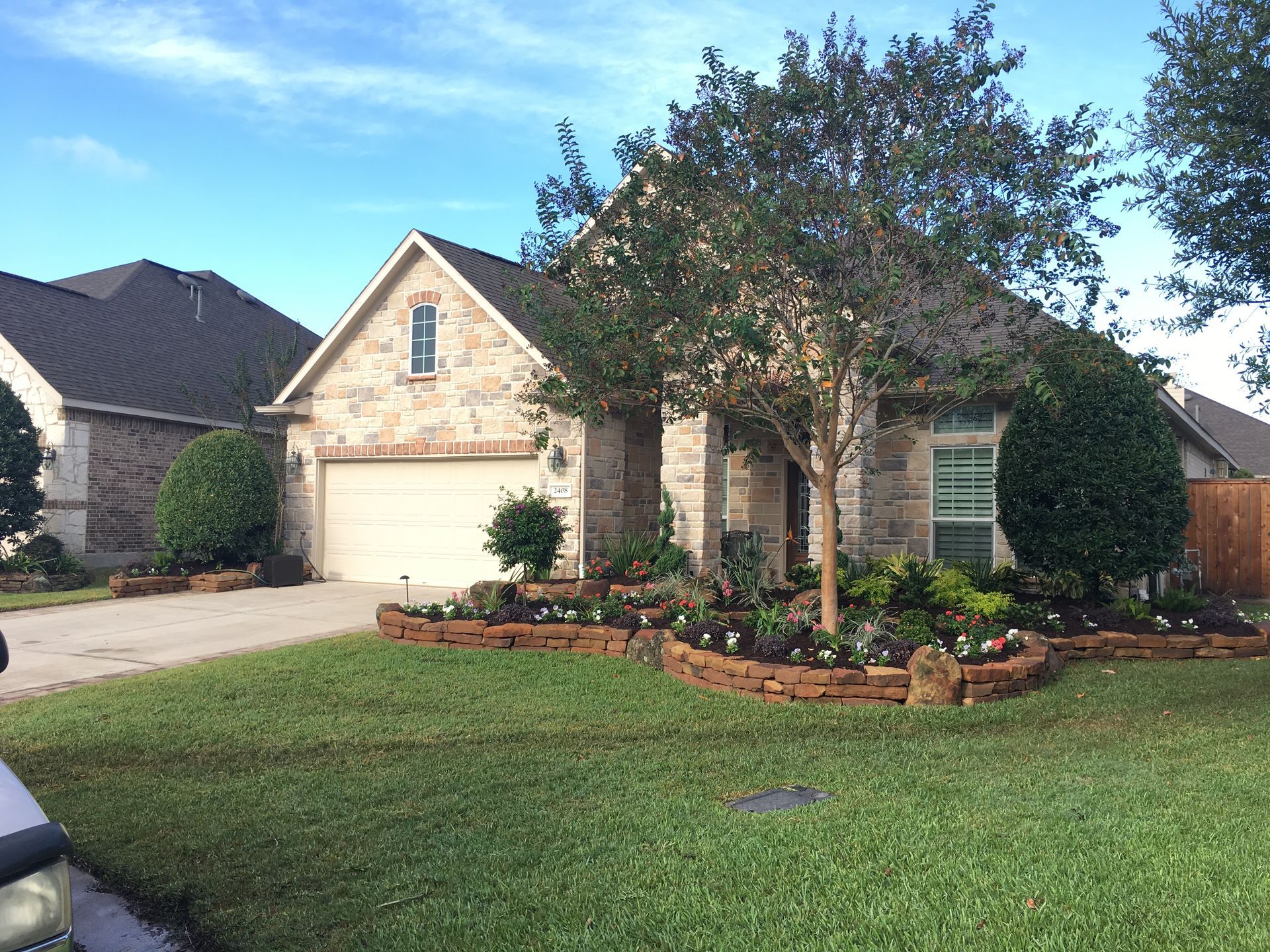 Suburban brick house with a two-car garage, manicured lawn, and landscaped front yard.