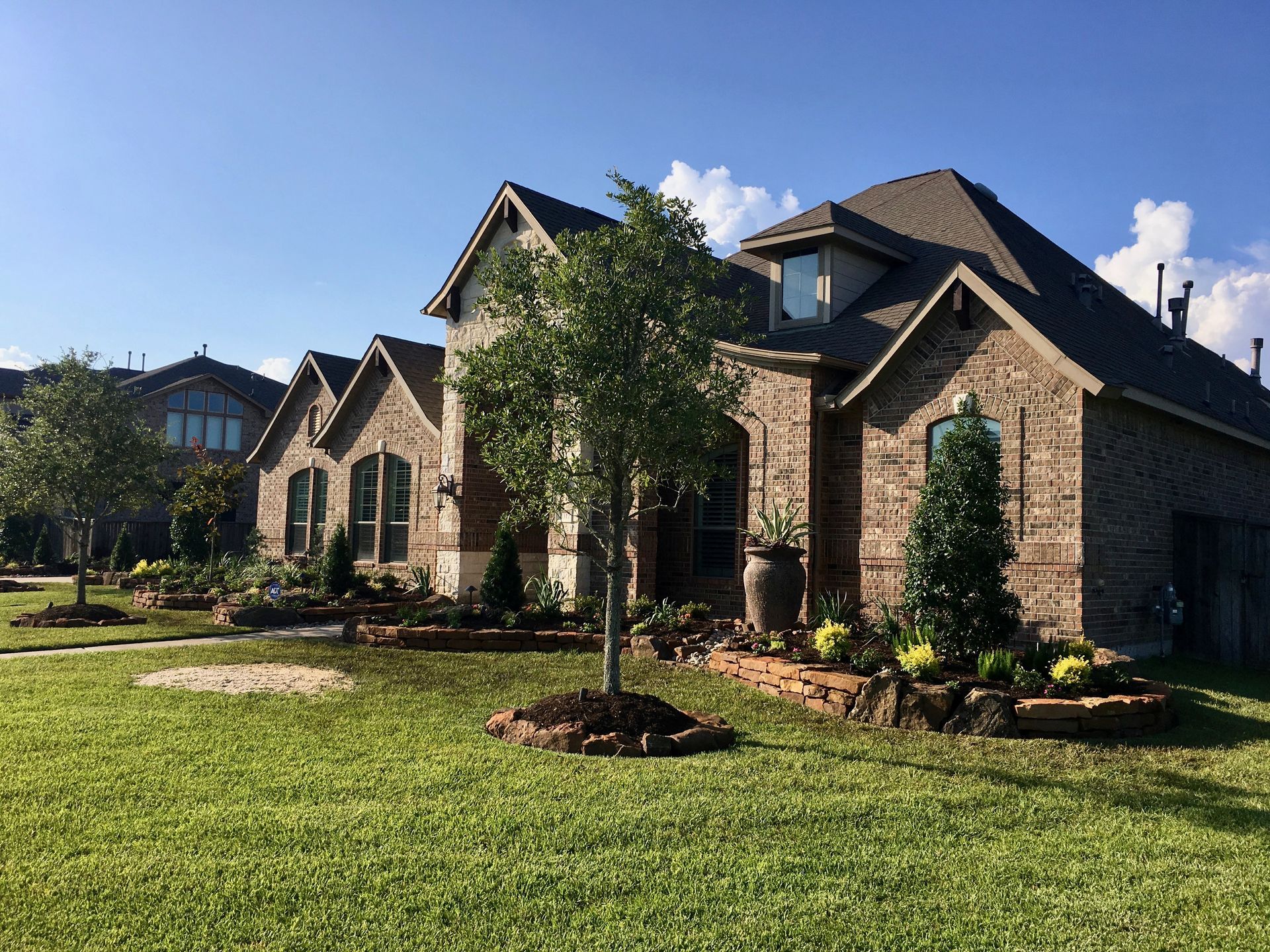 Brick suburban house with manicured lawn and young trees under a clear blue sky