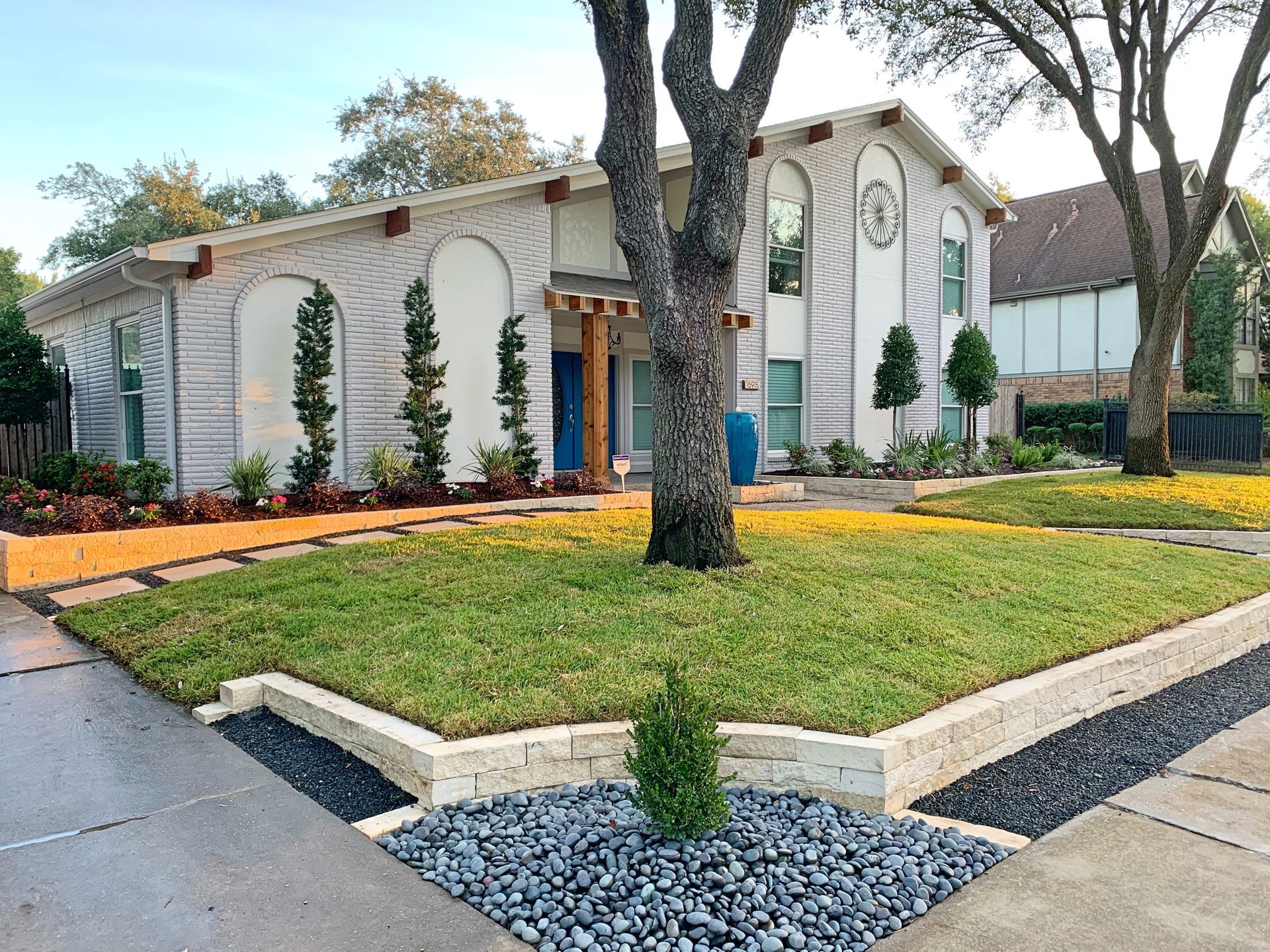 Modern white house with arched entry, landscaped front yard, and large tree at curbside