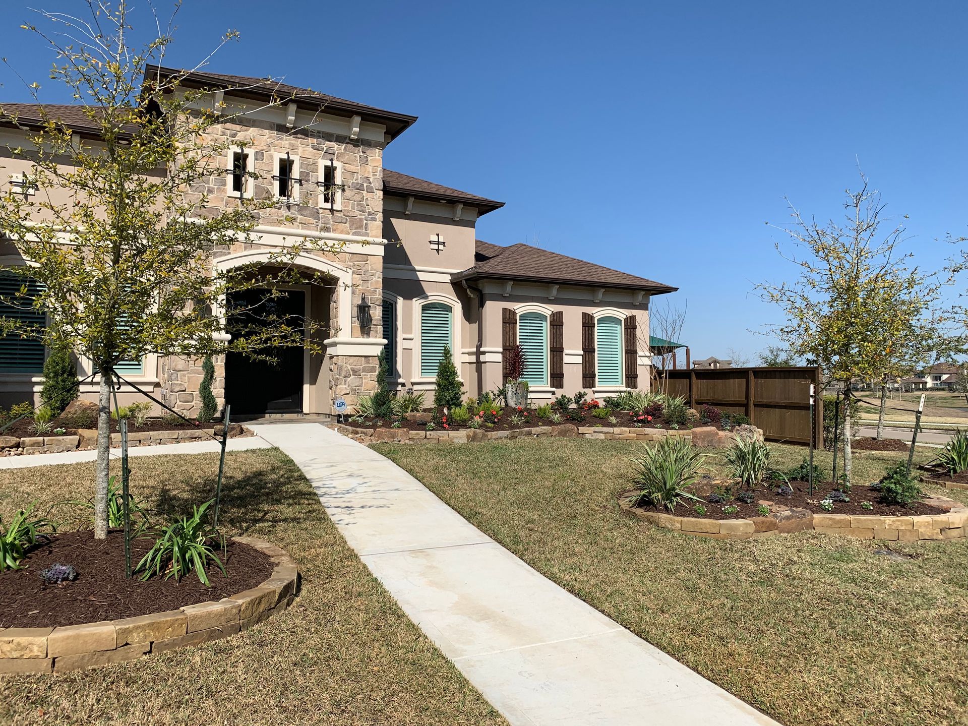 Suburban two-story house with stone facade, landscaped yard, and a concrete walkway under a clear blue sky